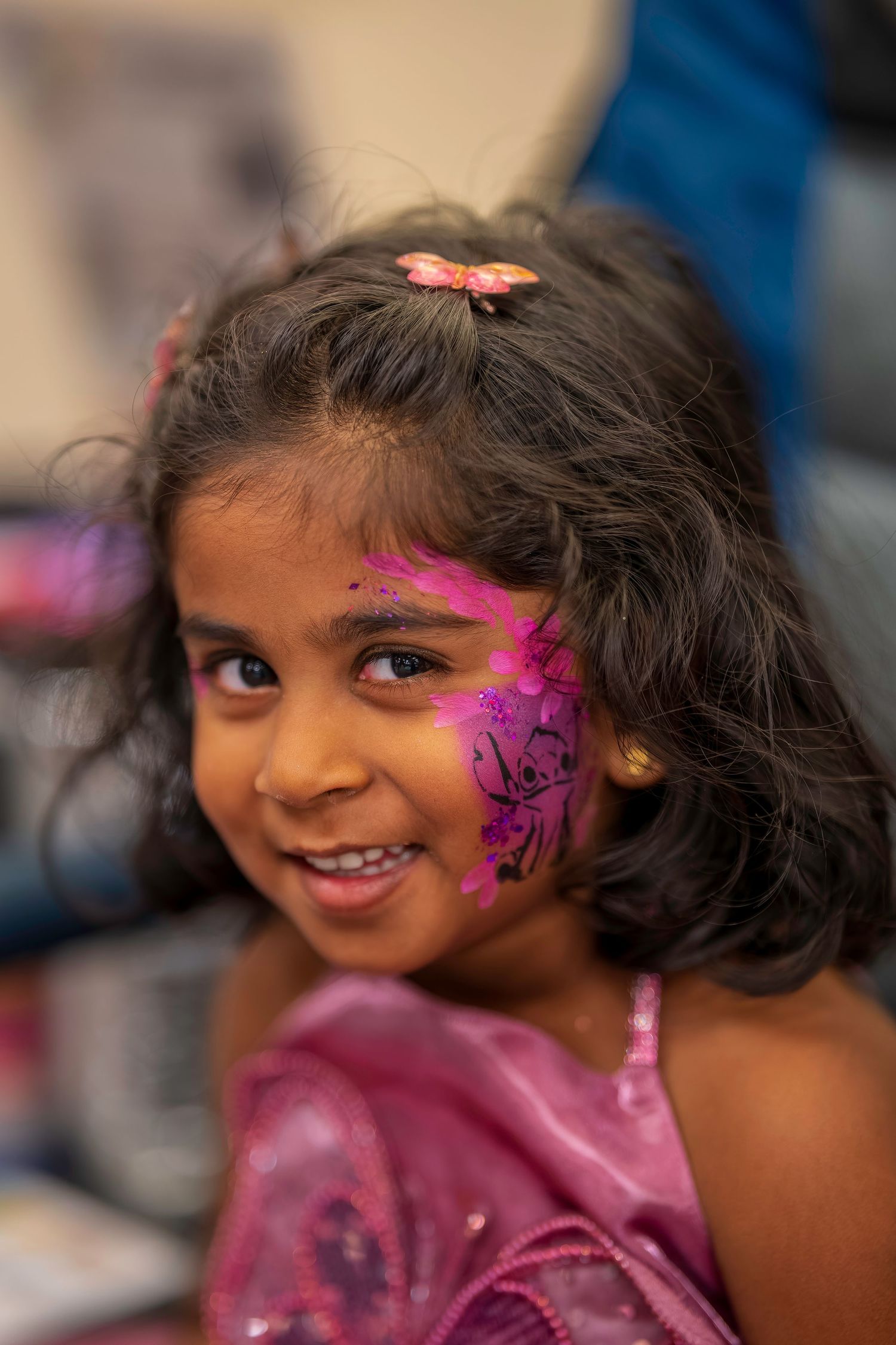 Young girl with pink and purple Stitch face paint smiling at birthday party.