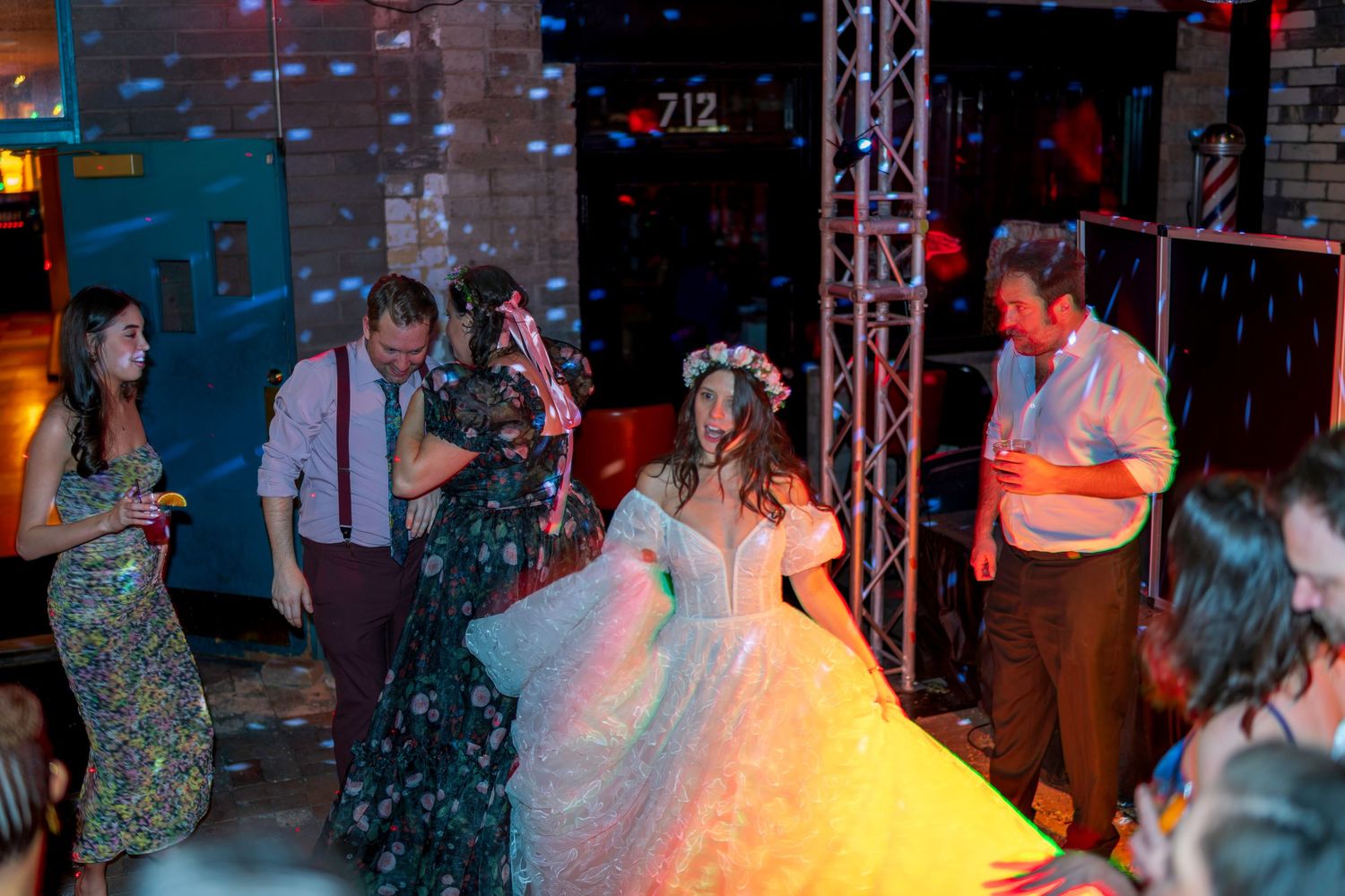 Bride in a colorful ball gown dancing with guests at a vibrant wedding reception party.
