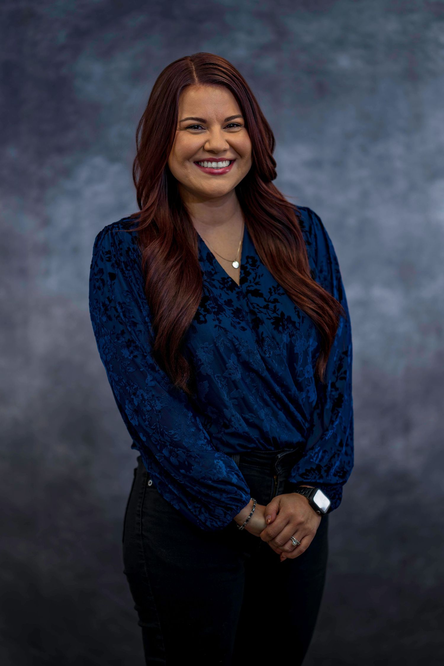 Professional studio portrait in navy blue top against dark background.