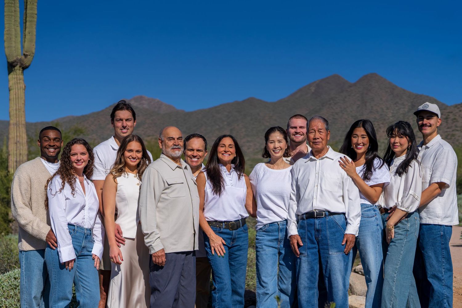 Group photo of people in coordinated white and denim outfits with desert mountains in background.
