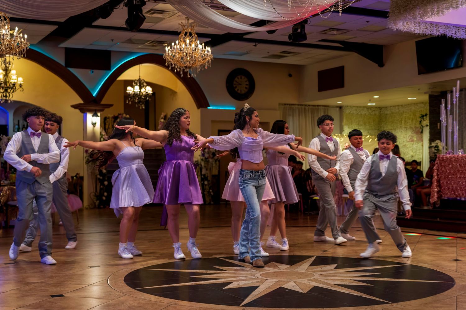 Teens in purple dresses and gray suits perform a choreographed dance at an elegant quinceañera celebration.