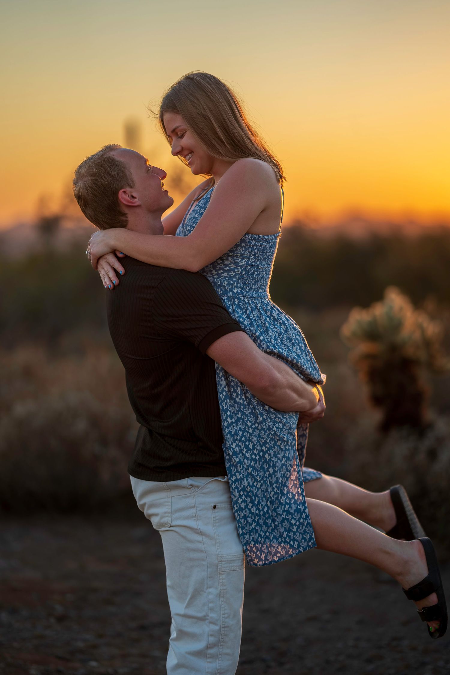 Couple sharing a romantic sunset moment as man lifts woman in desert landscape.