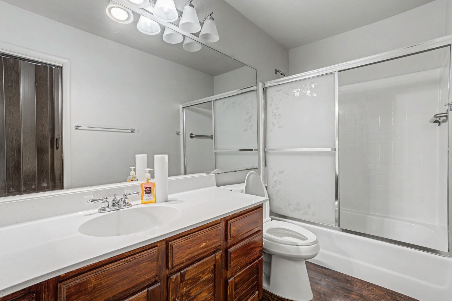 Full bathroom featuring wood vanity, white countertop, toilet, and glass-enclosed shower-tub combo.
