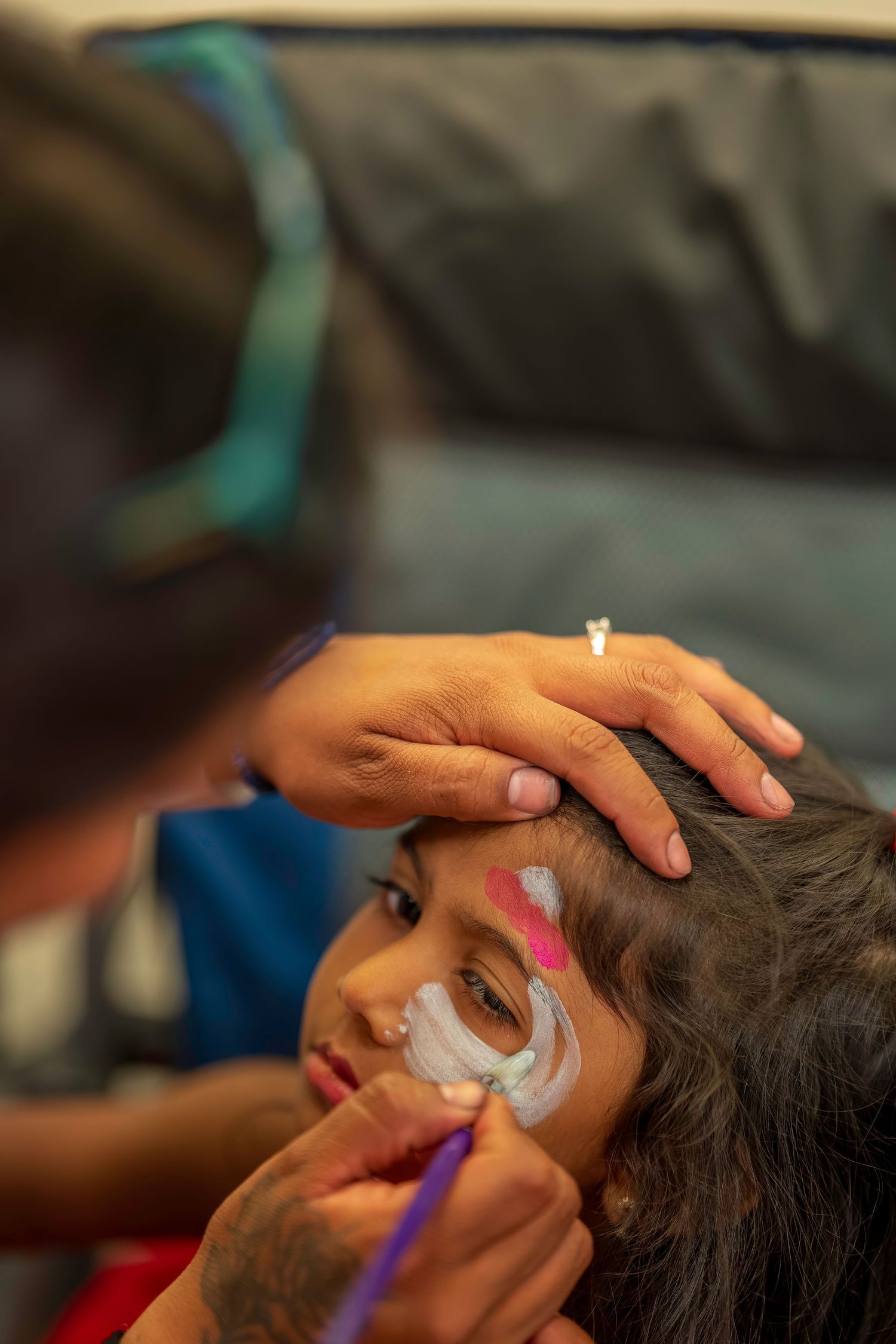Artist applying white face paint on a young girl's face with a brush at a children's event.