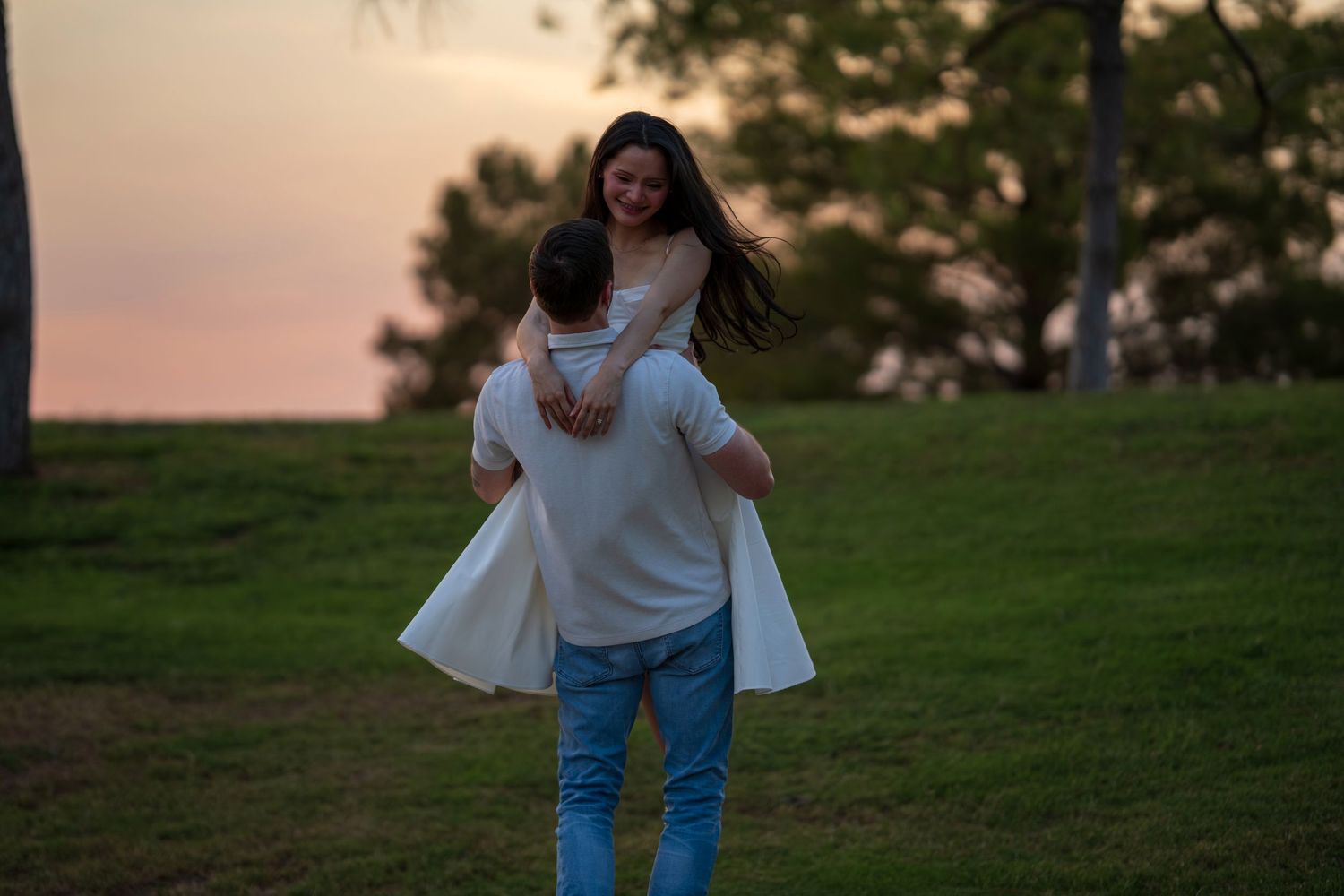 A groom twirls his bride in a green park field during a romantic sunset wedding photo.