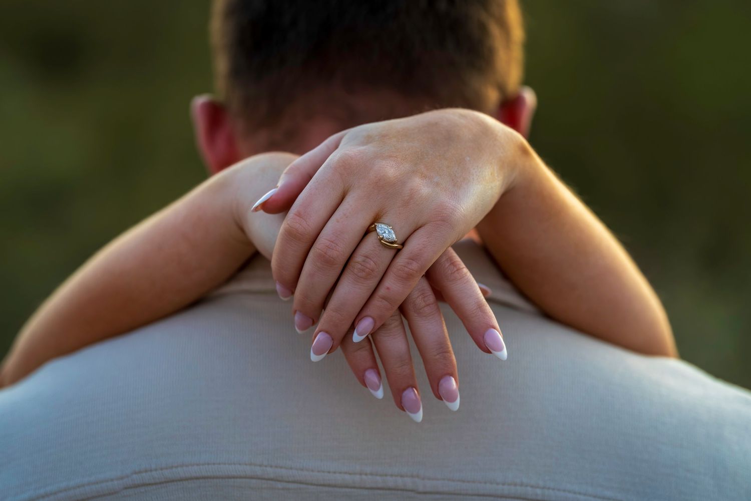 Close-up of a woman's hand with a diamond engagement ring resting on a man's shoulder.