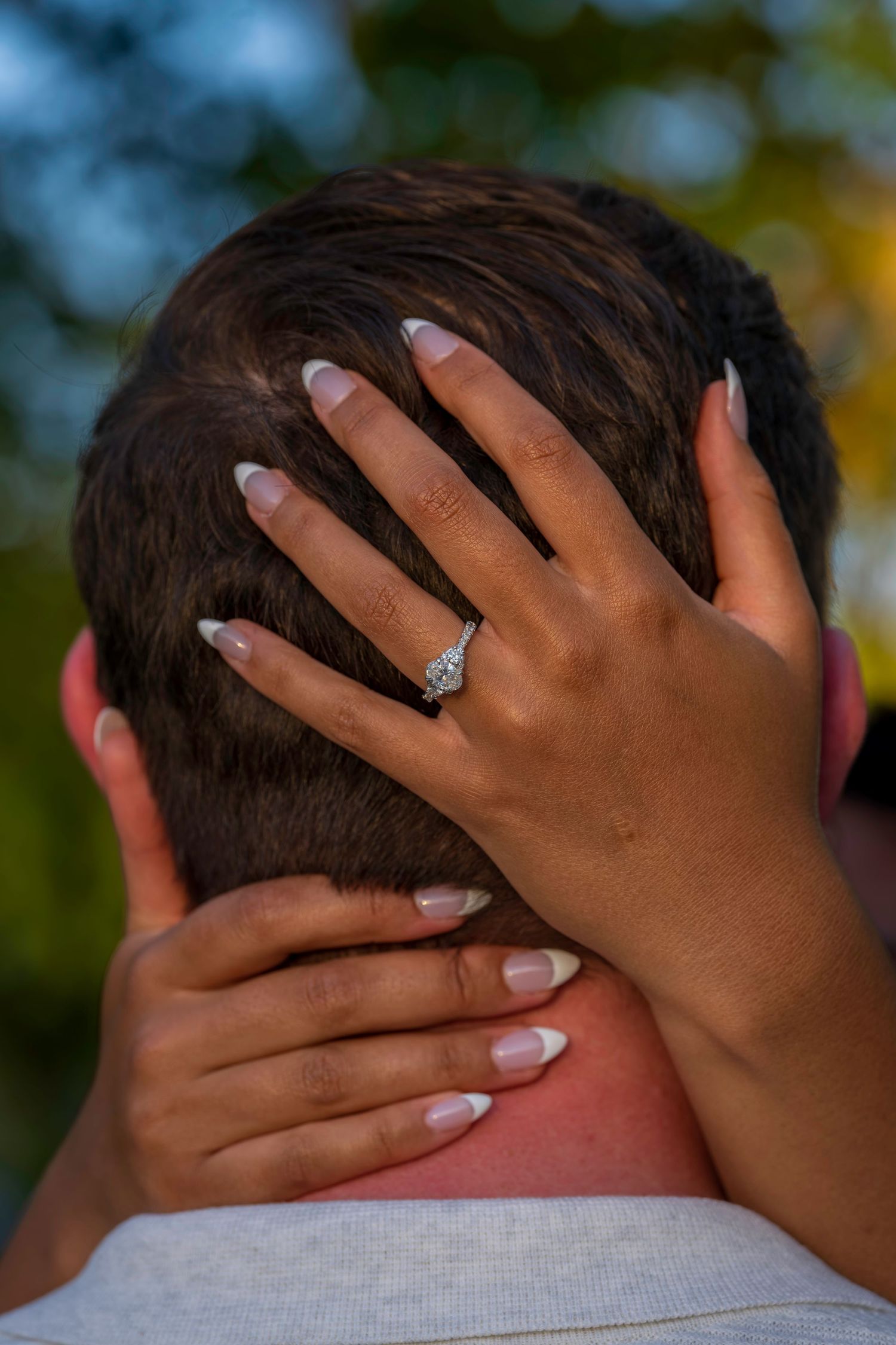 Close-up of a woman's hand with French tip nails and diamond engagement ring resting on a man's head.