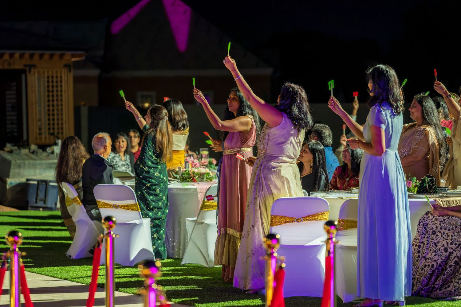 Guests in formal attire dancing with raised arms at an outdoor evening celebration.