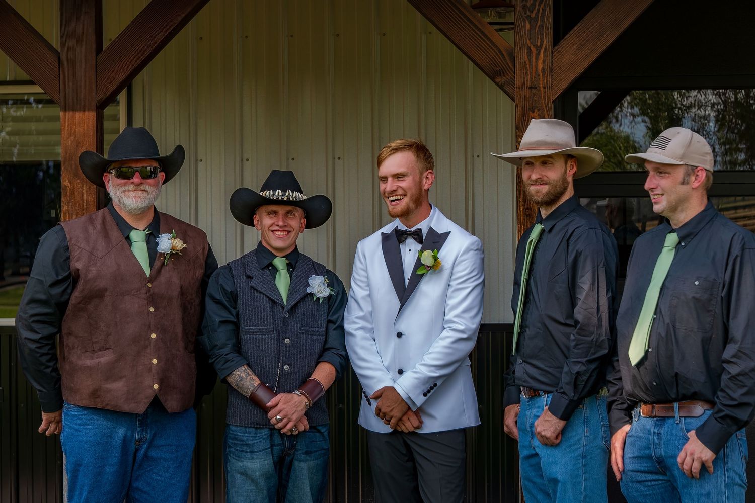 Groomsmen in western attire and cowboy hats pose at a rustic wedding venue.