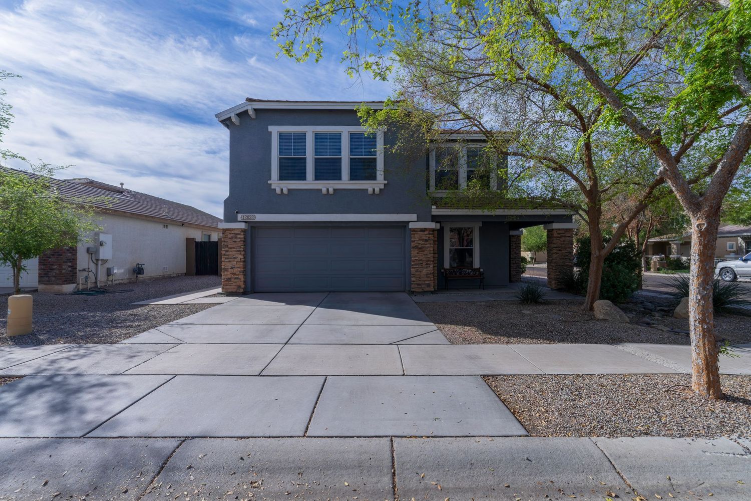 Two-story gray home with stone accents, two-car garage, concrete driveway, and desert landscaping.