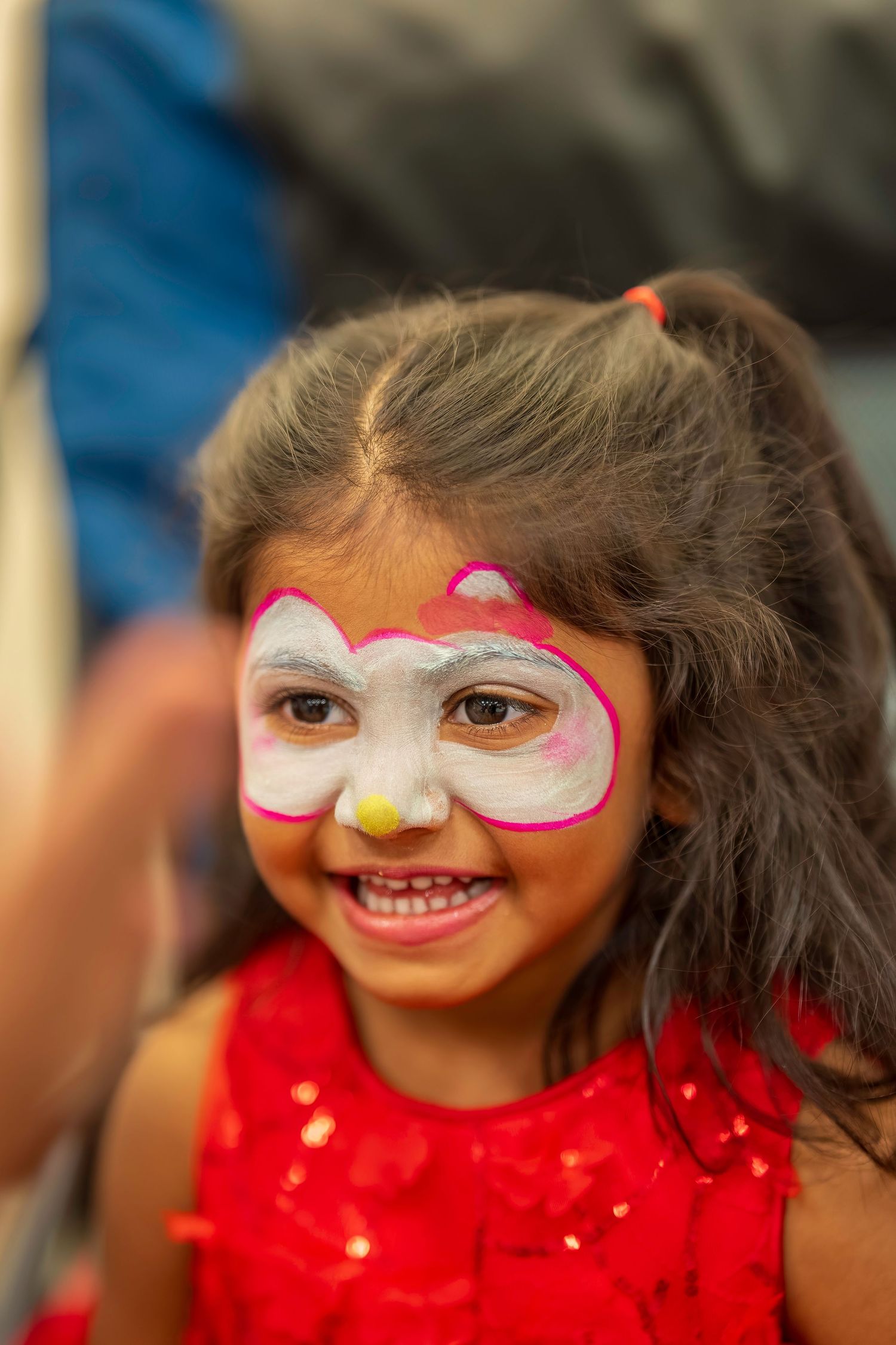 Smiling little girl with Hello Kitty face paint wearing red dress at party.