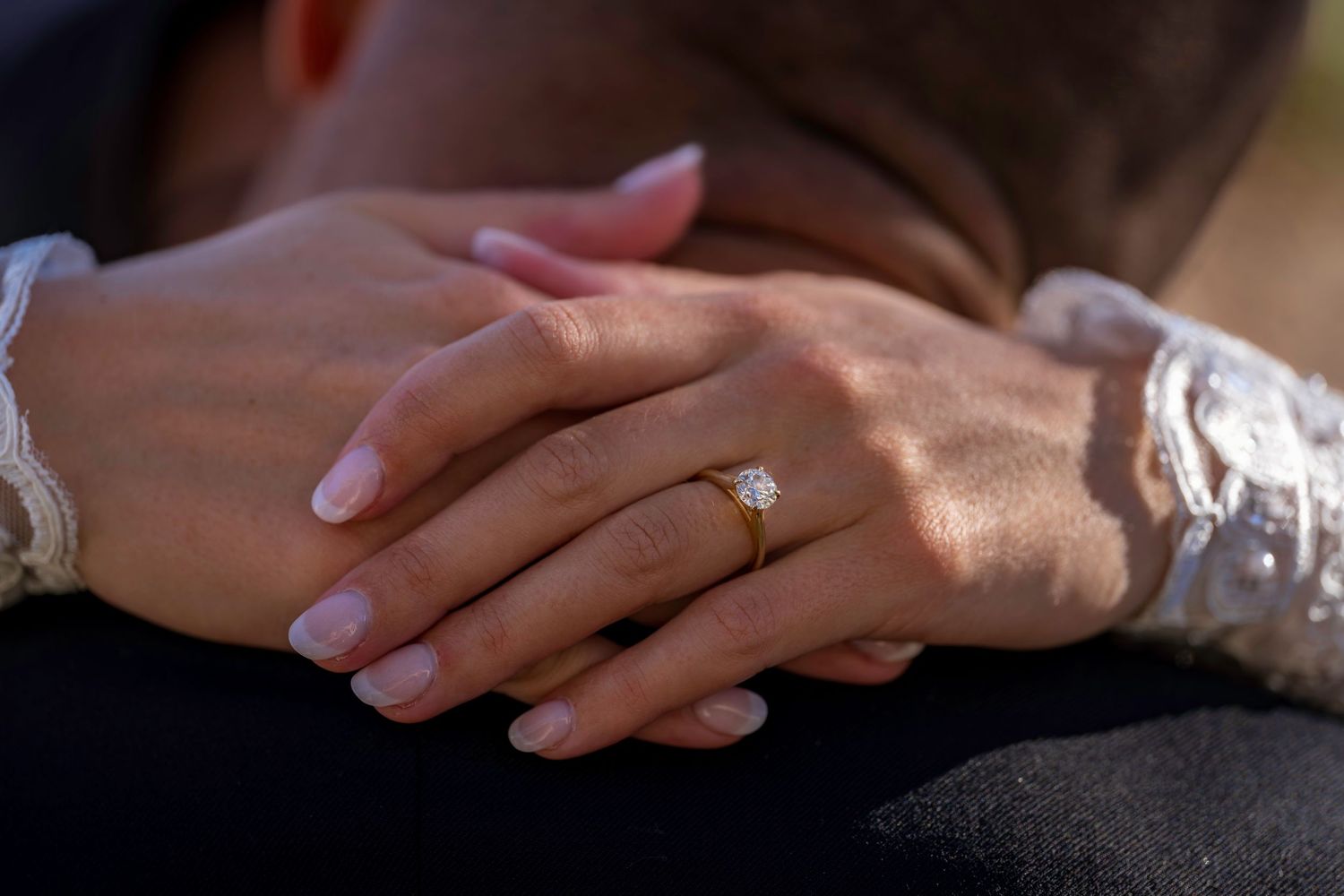Close-up of bride's hand resting on groom's arm showcasing gold diamond engagement and wedding ring.
