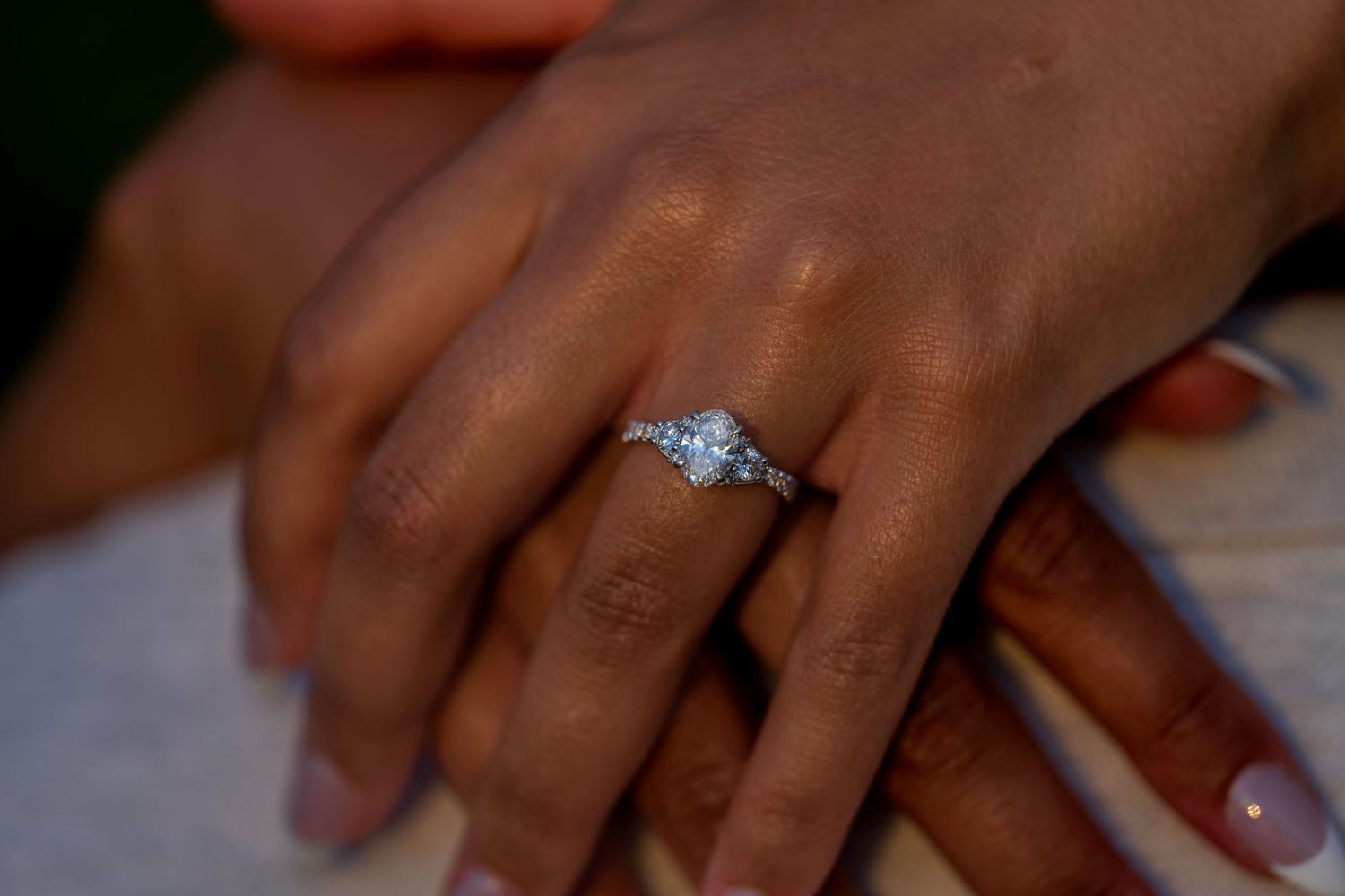 Close-up of a diamond engagement ring on a woman's finger resting on a man's hand.