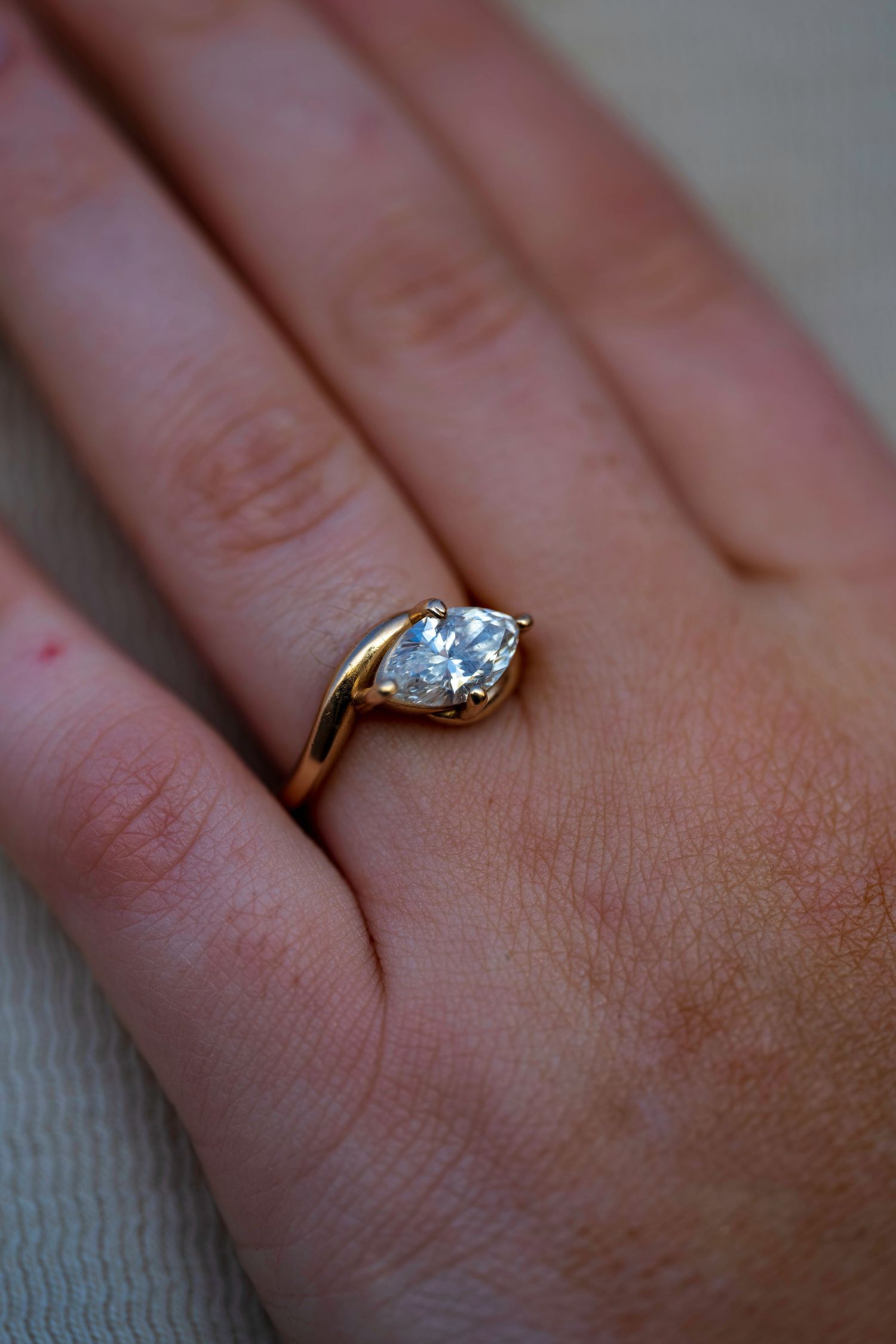 Close-up of a gold engagement ring with a heart-shaped diamond solitaire on a woman's hand.