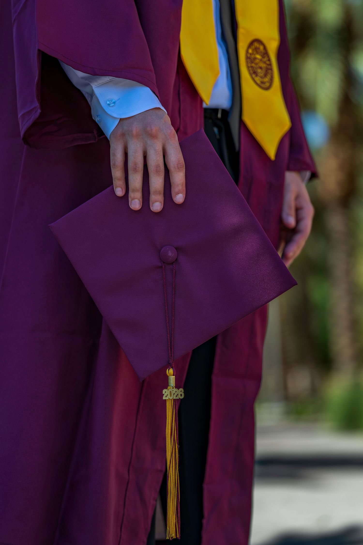 Graduate in maroon ASU regalia holding a graduation cap with a gold 2026 tassel in hand.