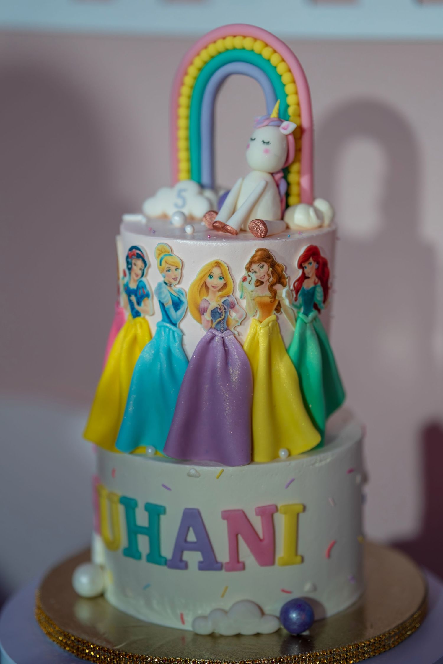 Disney princess themed birthday cake with rainbow topper and unicorn decoration.
