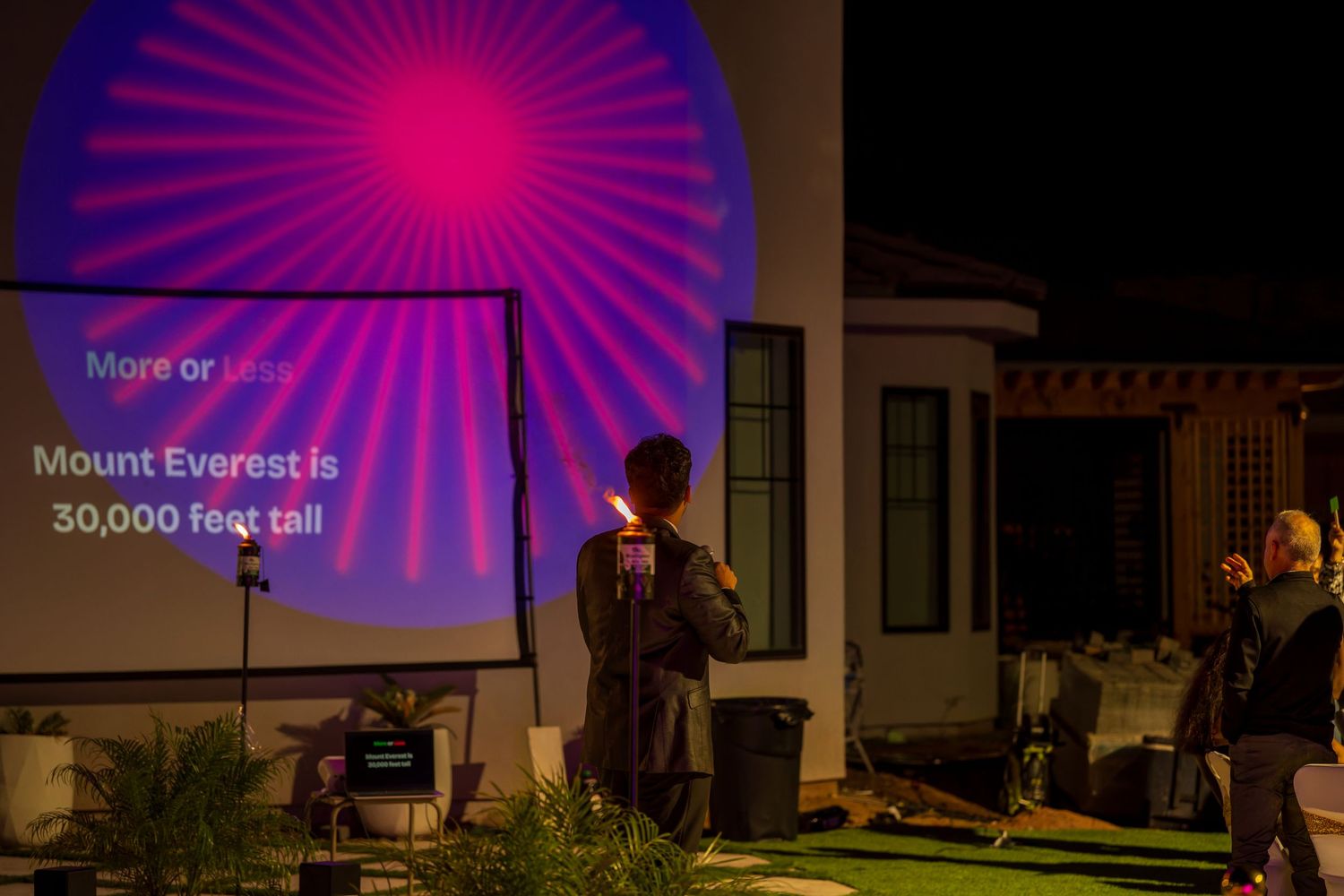 A pink radial projection illuminates the side of a building during an evening event.