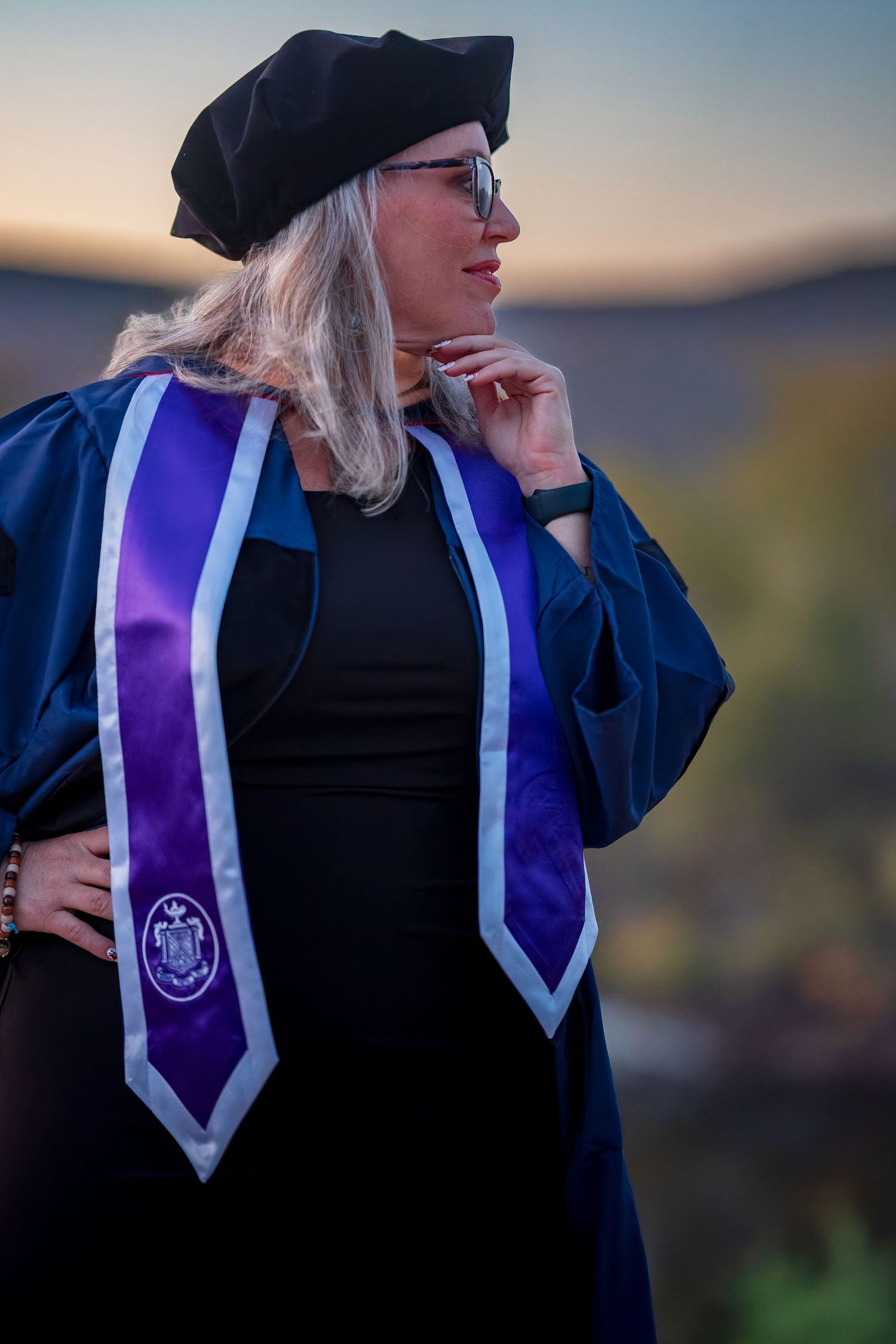 Academic regalia with purple and white stoles shown against sunset backdrop.