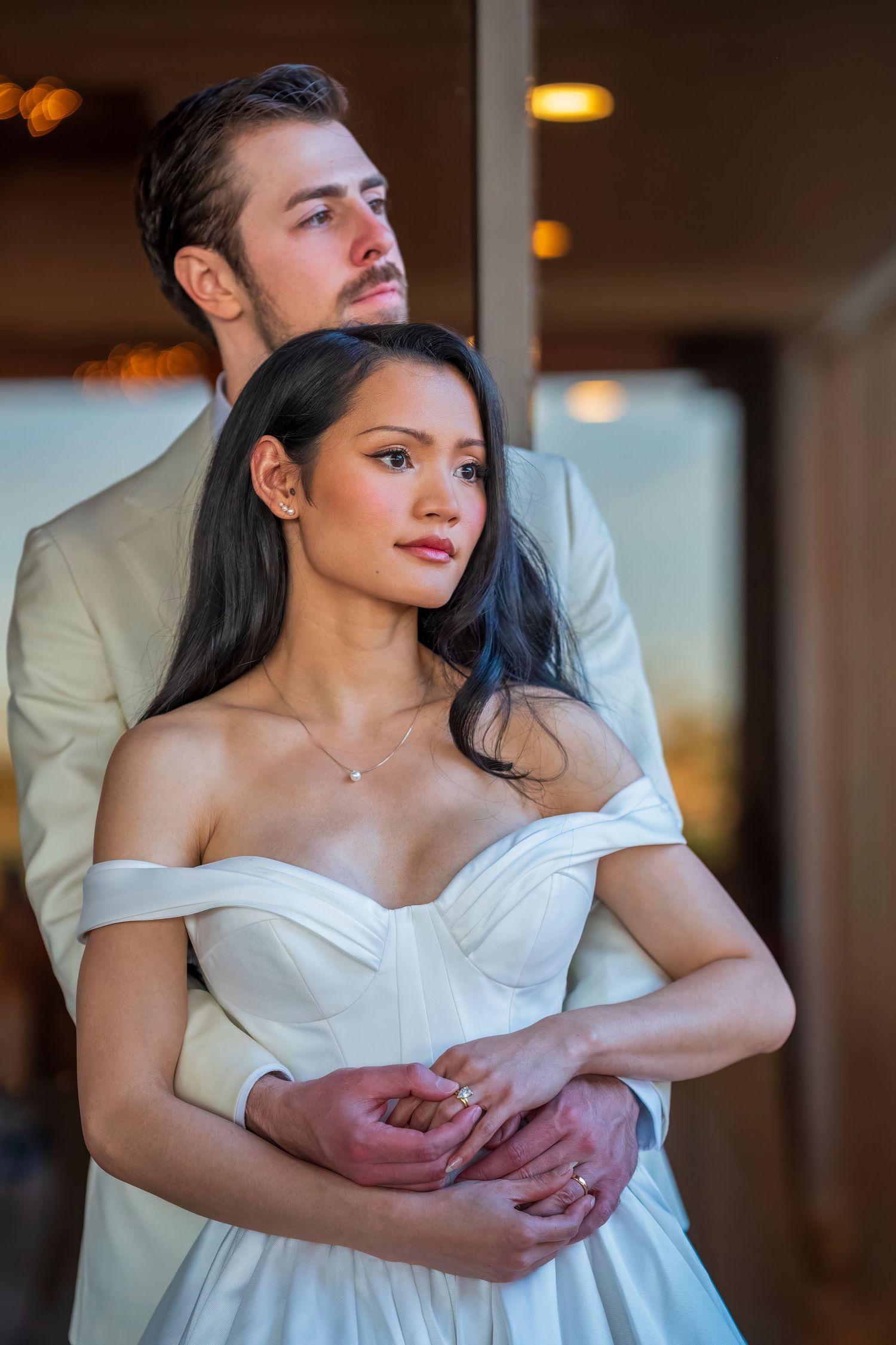 Tender embrace between couple in elegant wedding attire indoors.