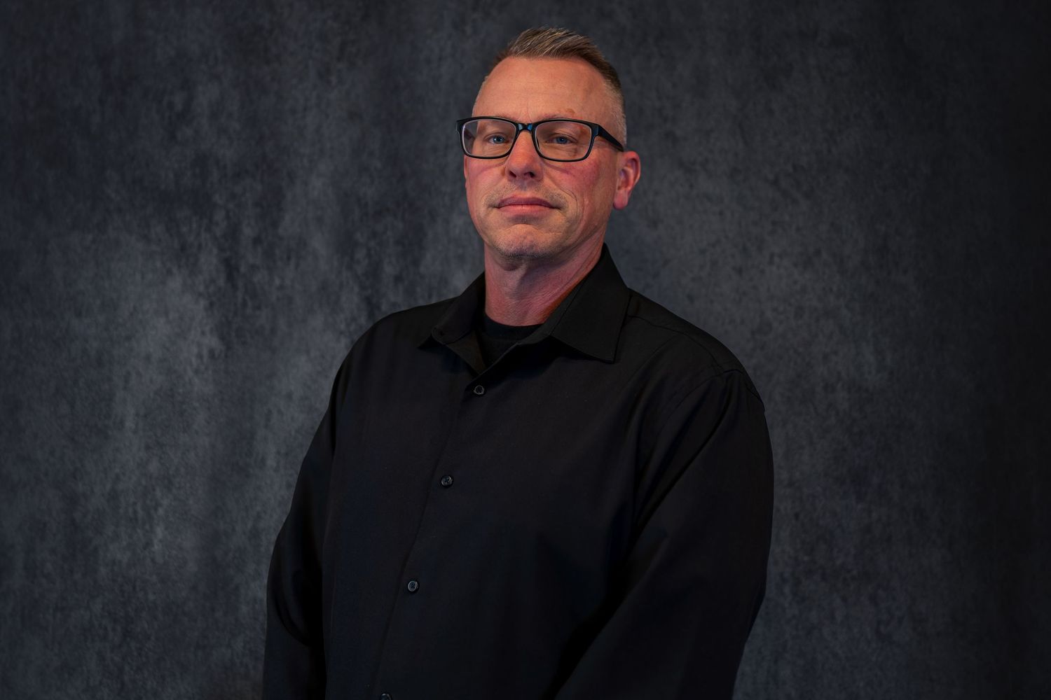 Business portrait of person in black attire against textured dark backdrop.