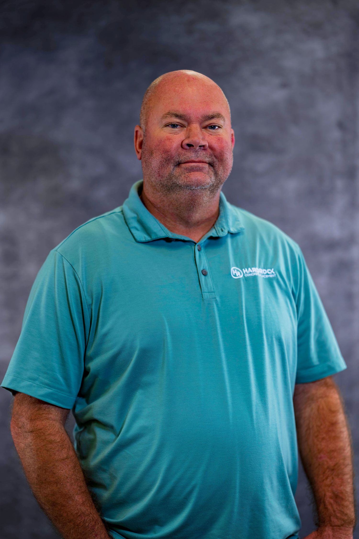 Person in teal polo shirt poses for professional headshot against textured background.