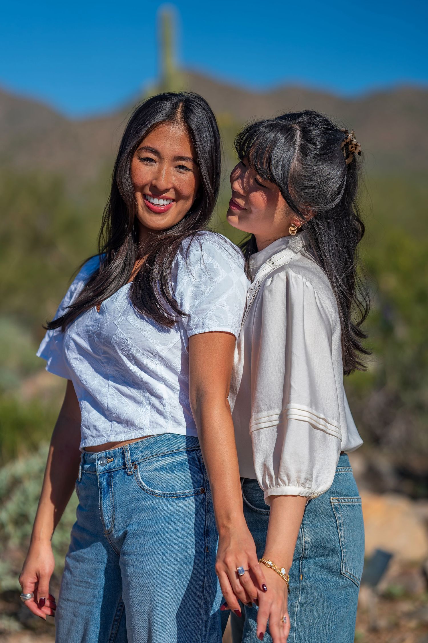 Two friends in matching denim and white tops laugh together in a desert landscape.