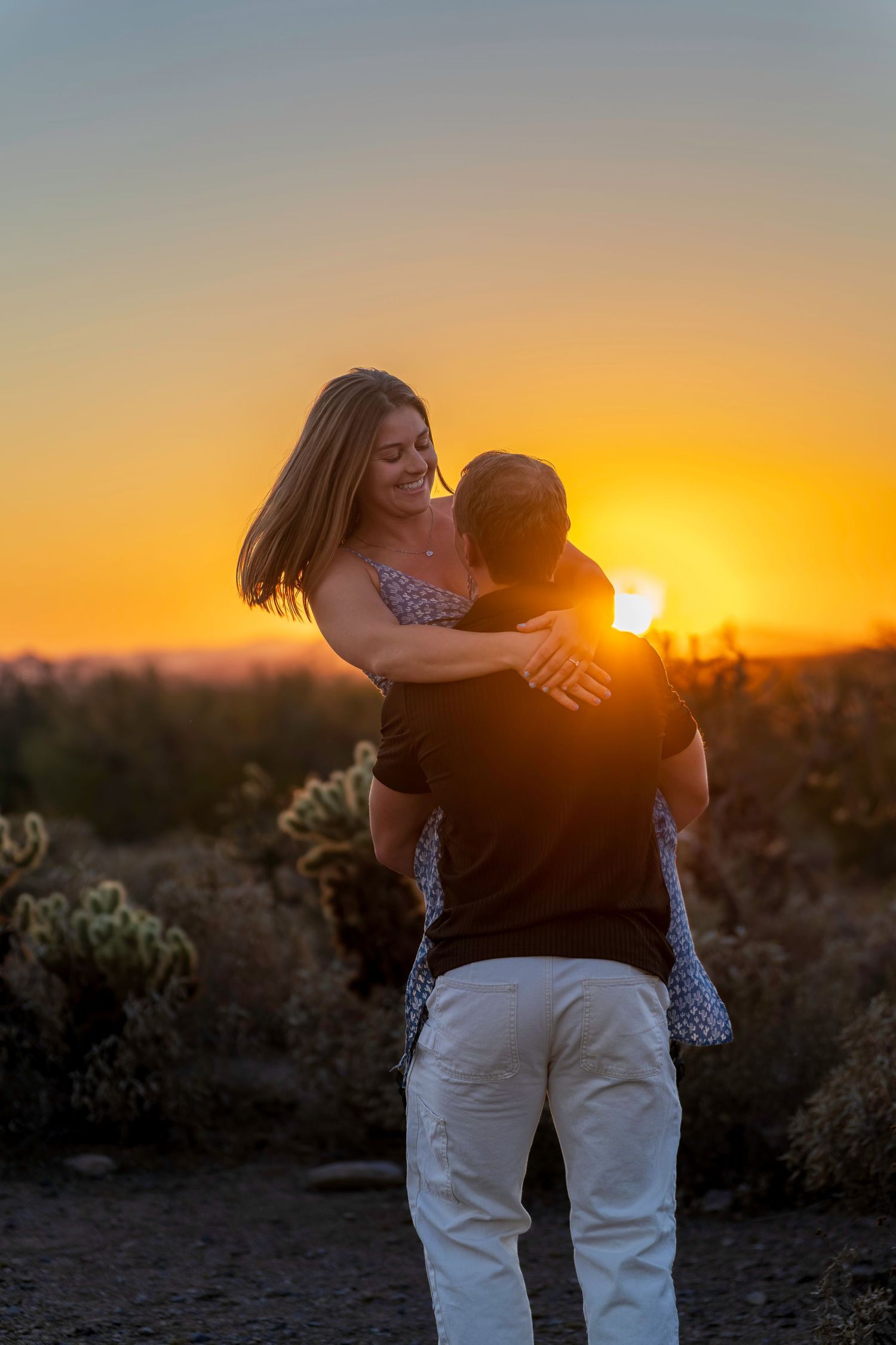 Couple embracing at golden sunset in desert landscape with cacti, romantic outdoor photography.