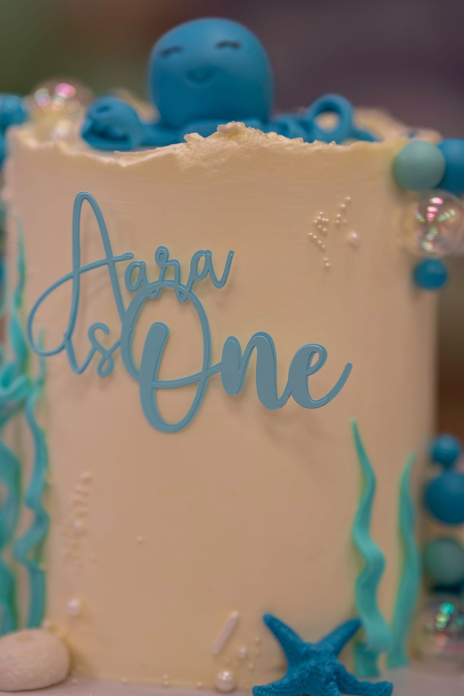 Ocean-themed first birthday cake with blue octopus topper reading Aara Is One.
