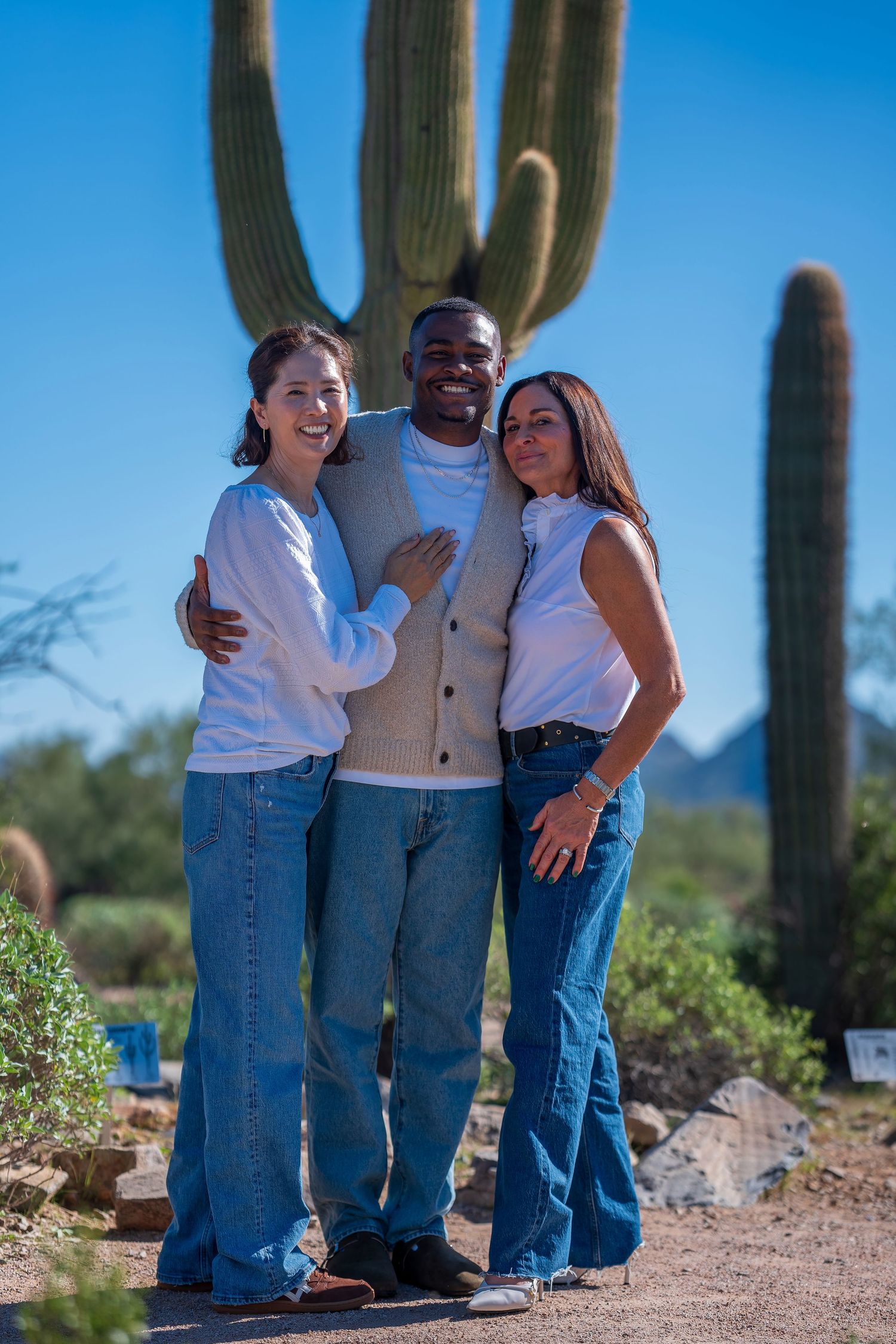 Casual group photo with people in coordinated white and denim outfits against desert scenery.