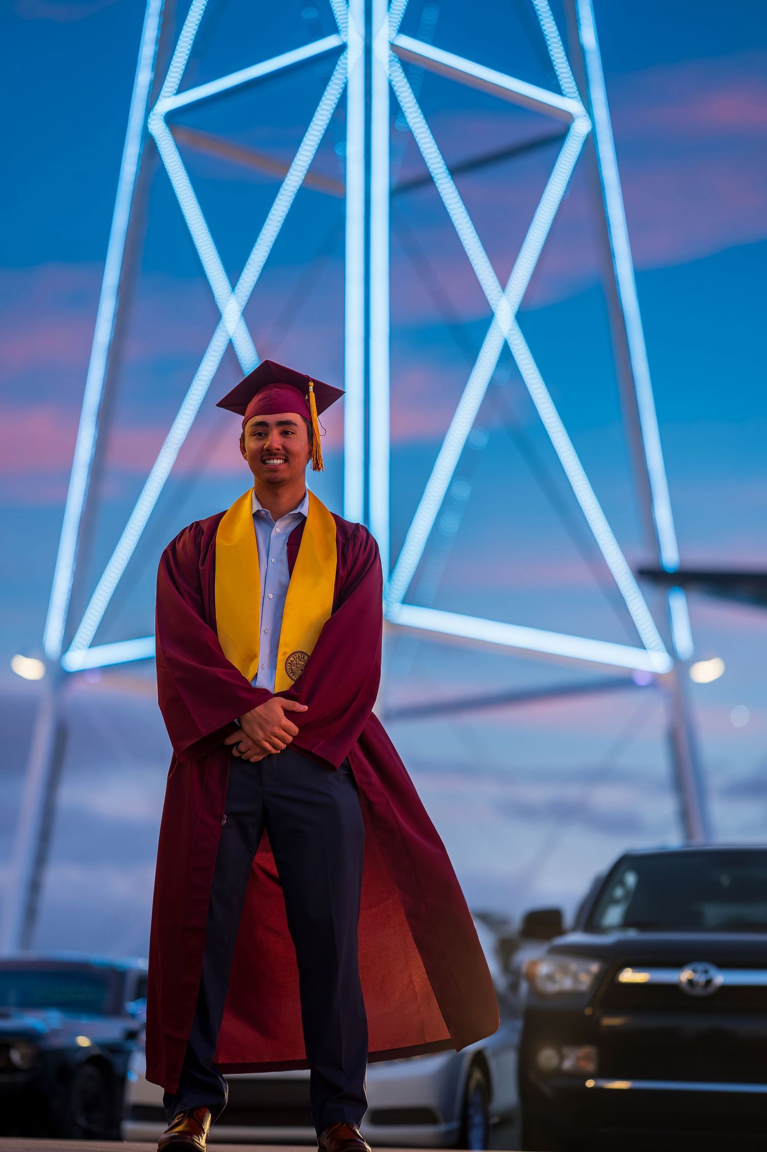 Graduate poses in front of lit-up water tower structure during blue hour.