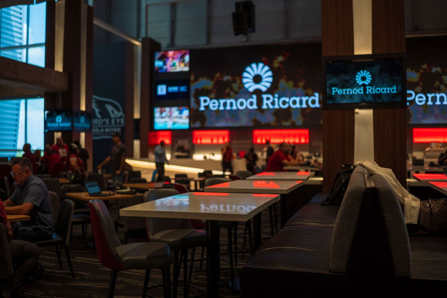 Dark bar interior with illuminated Pernod Ricard signage and ambient lighting.