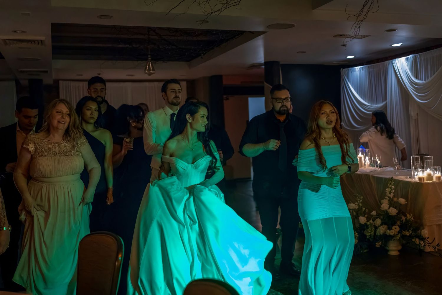 Wedding guests dance together under vibrant green lighting at a reception.