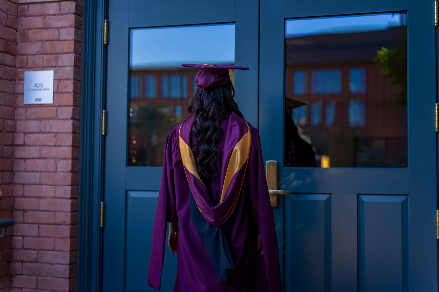 Graduate in academic regalia walks along pathway at sunset.