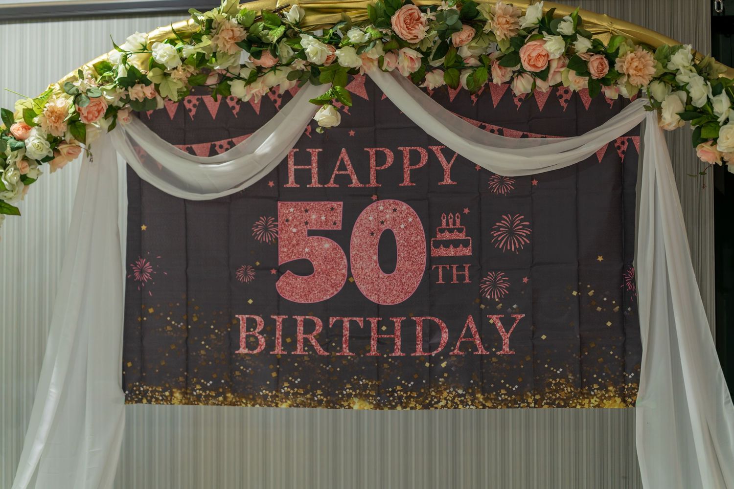 50th birthday celebration banner with floral decorations and white draping.