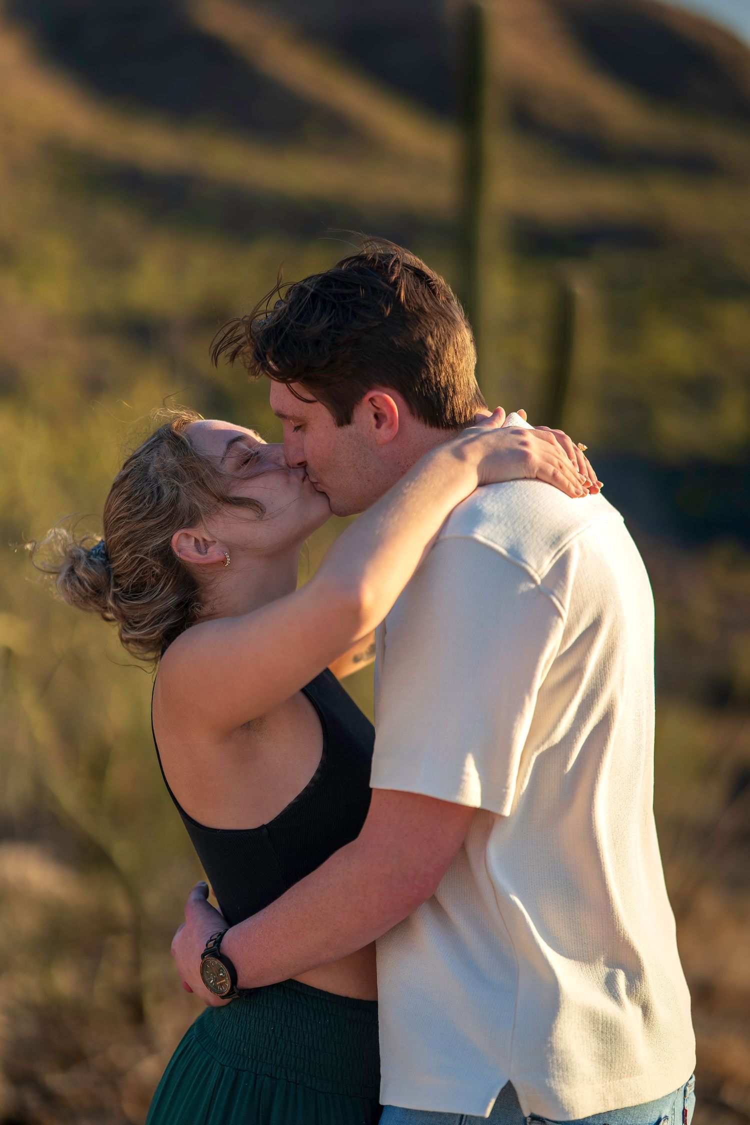 Romantic couple sharing a kiss outdoors in a sun-drenched desert setting with cacti behind them.