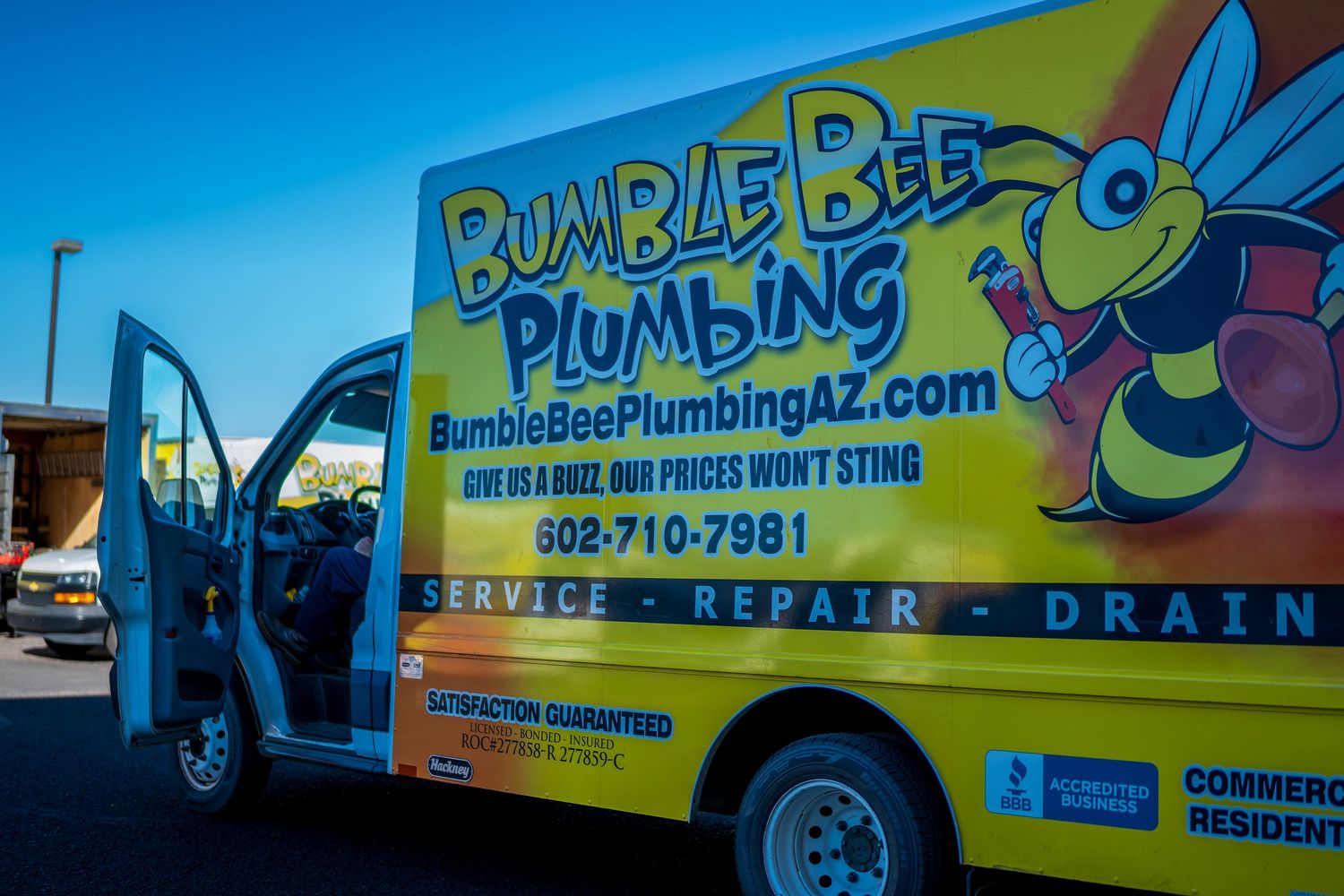 Bright yellow Bumble Bee Plumbing service van with cartoon bee logo parked outside.