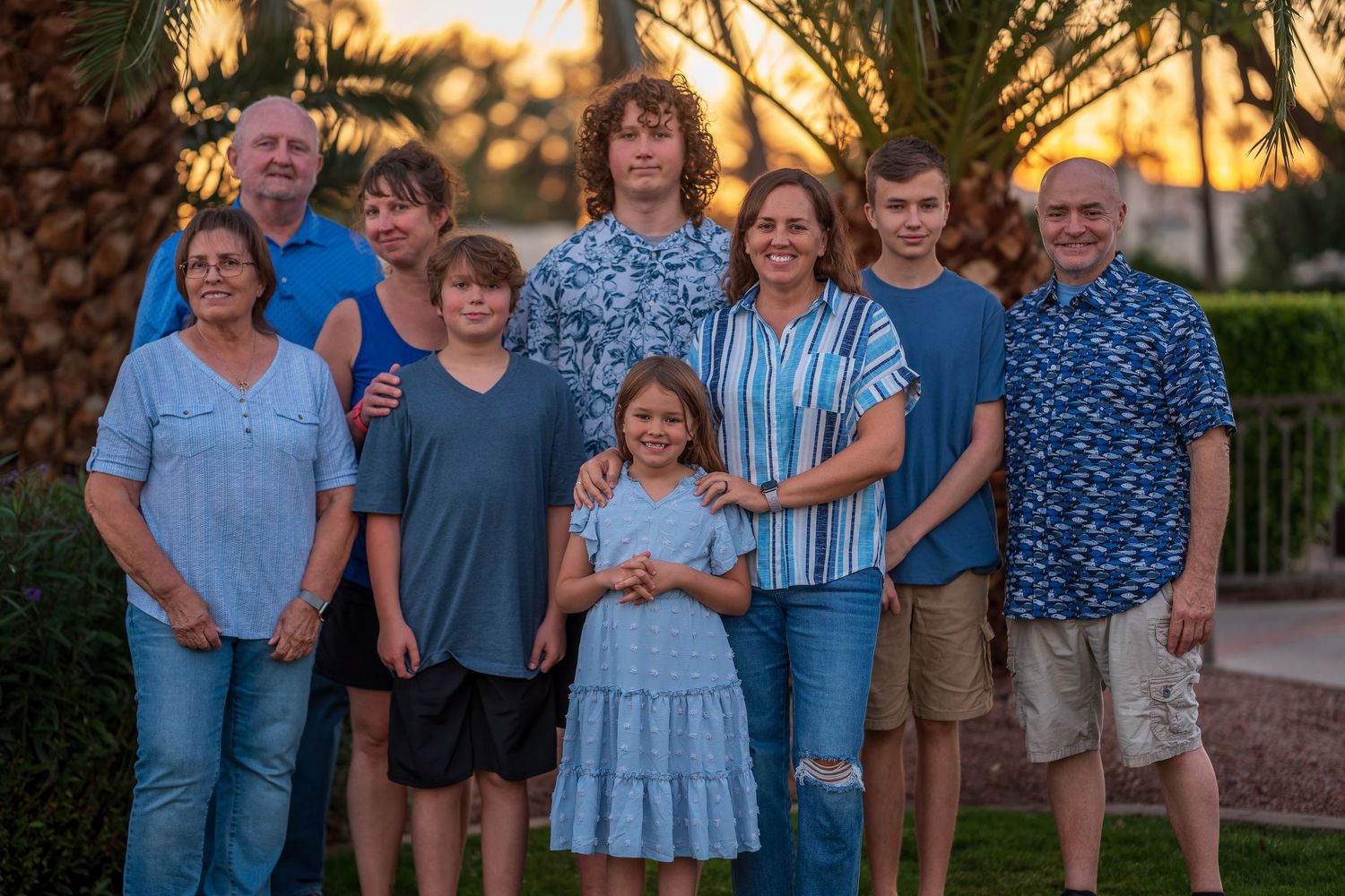 Group photo of family wearing coordinated blue outfits in front of palm trees at dusk.