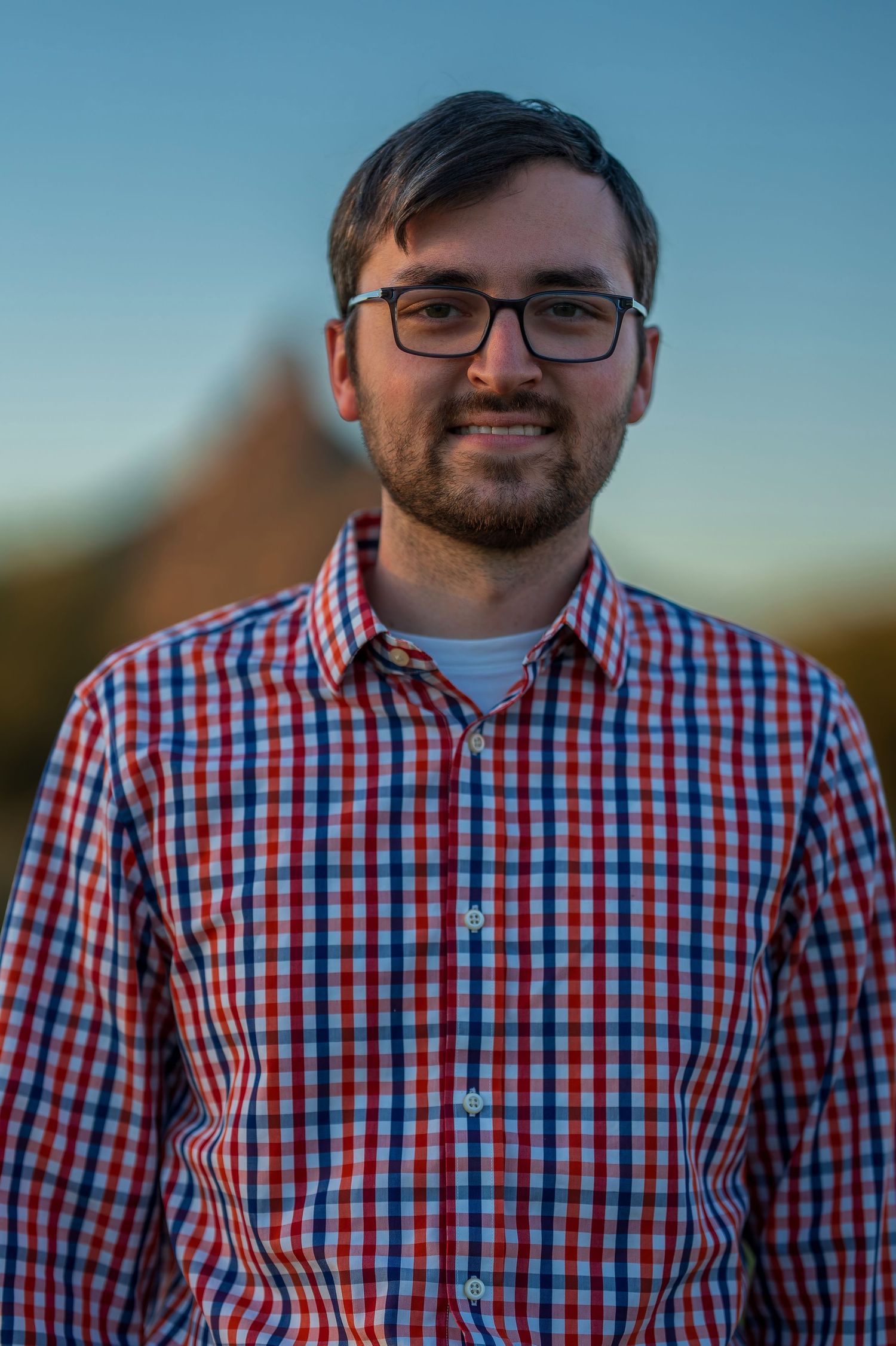 Close-up portrait of person in red and blue checkered button-down shirt against blue sky background.