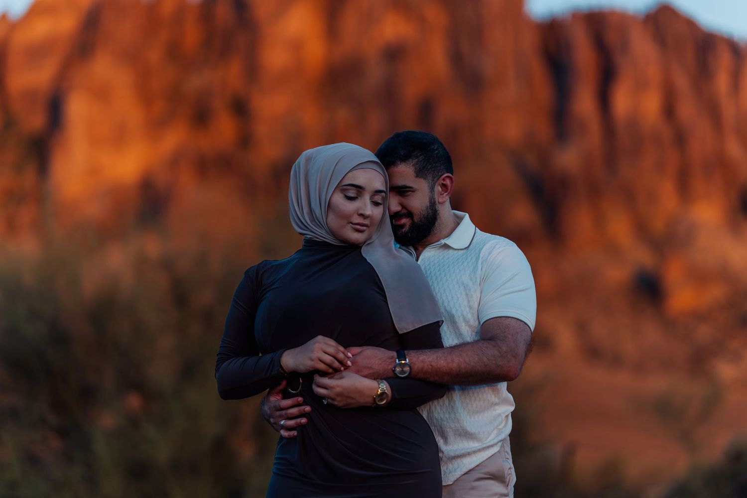 Couple embracing against stunning red rock formations at sunset.