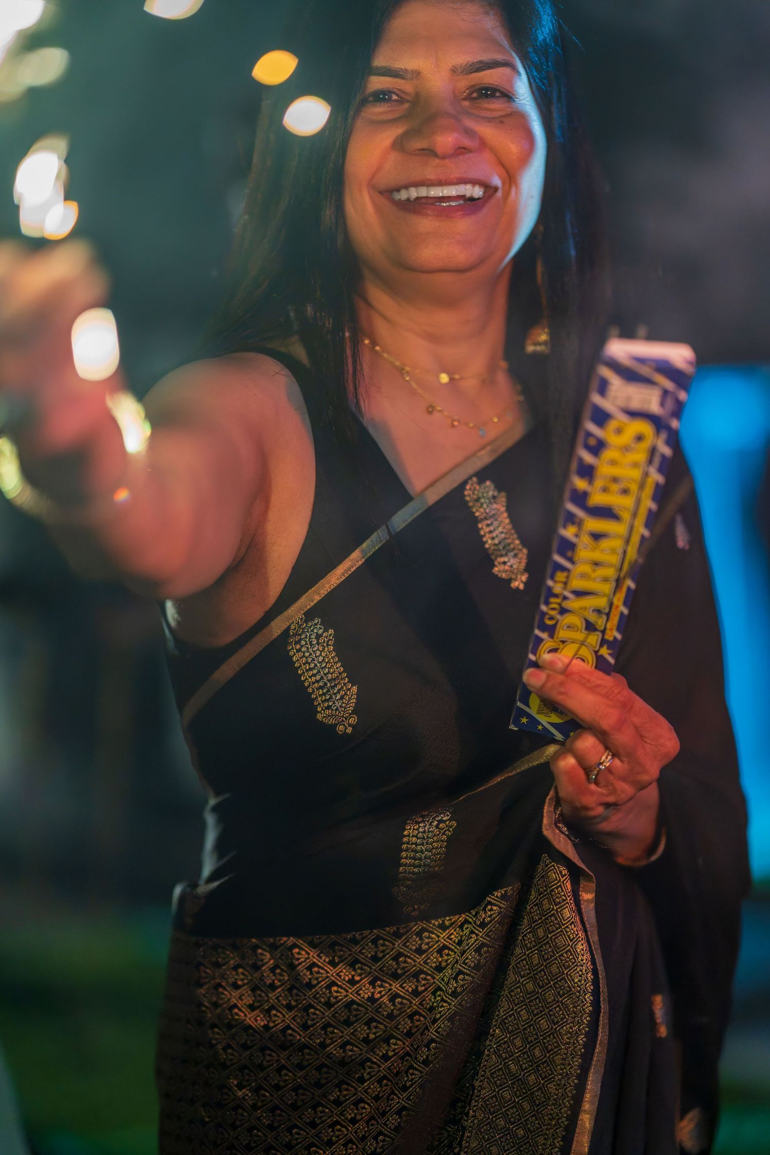Person in black outfit holds sparklers during nighttime celebration.