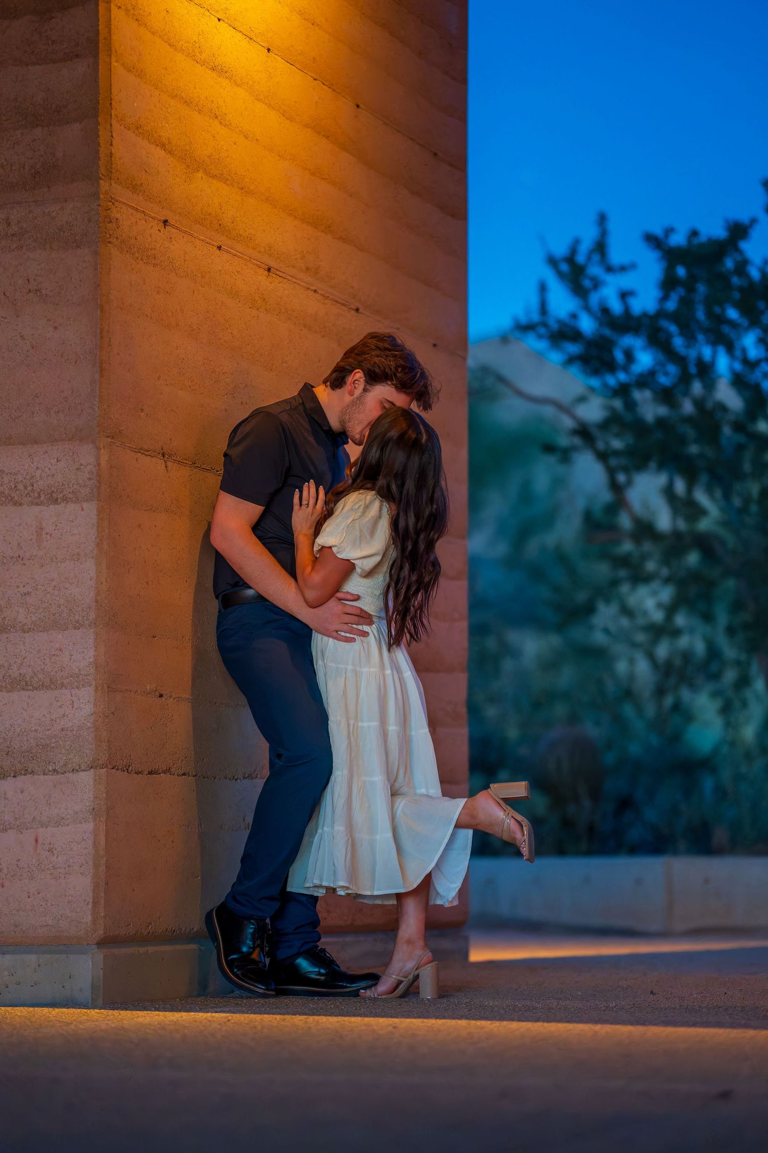 Intimate couple moment captured against warm-lit wall during evening photoshoot.