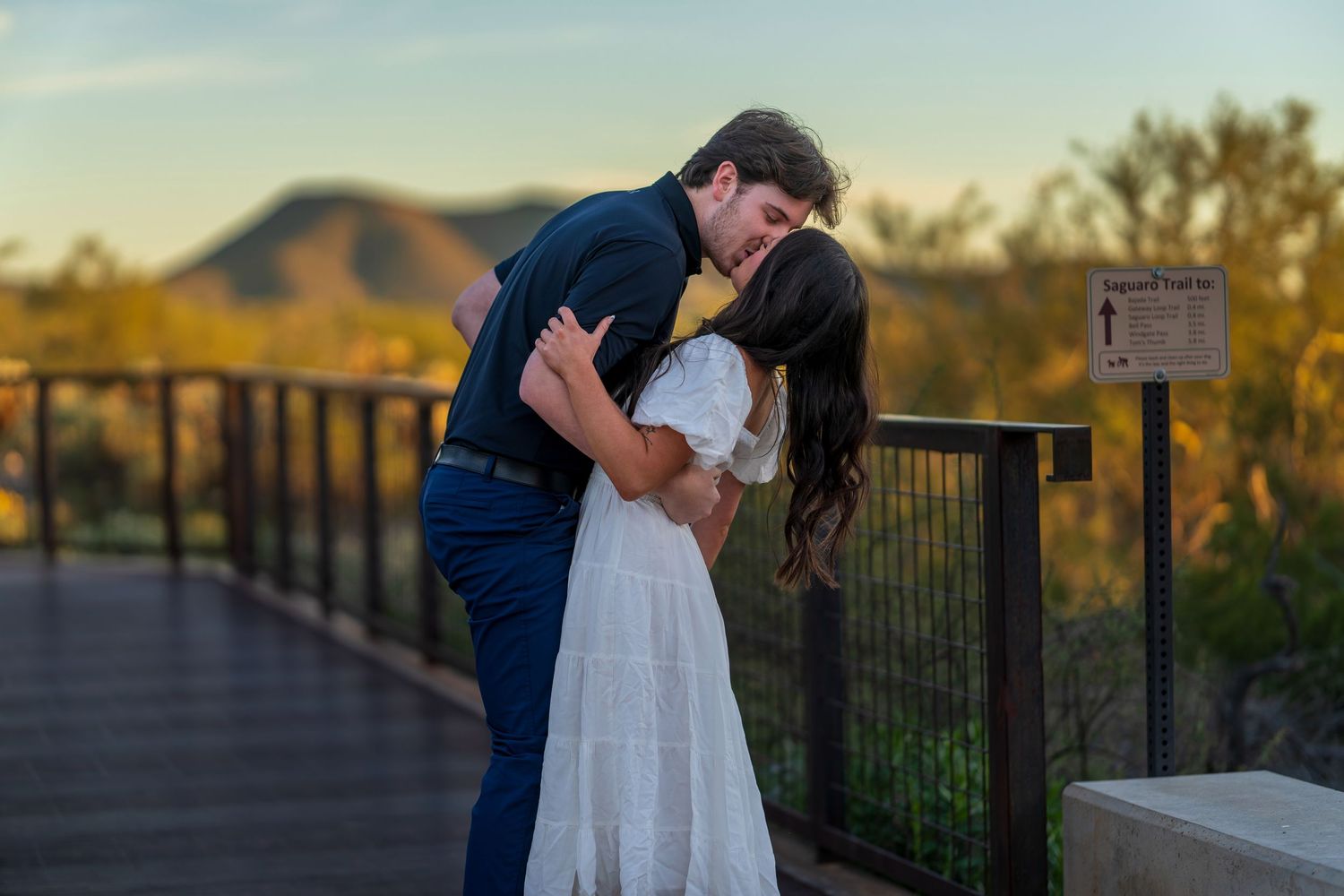 A newly engaged couple sharing their first kiss on a scenic overlook at sunset.