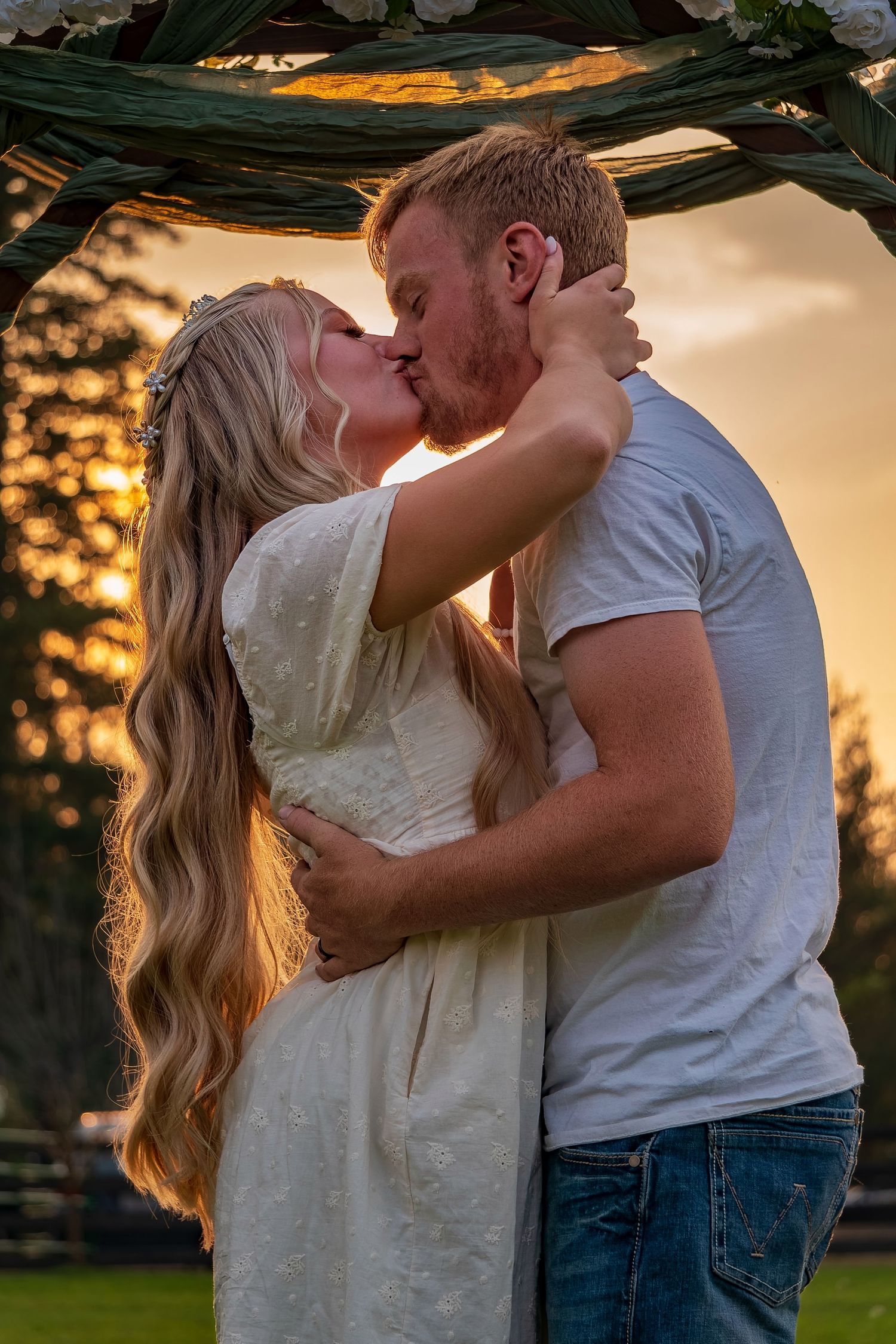Couple embracing in a passionate kiss beneath a decorated garden arch at dusk.