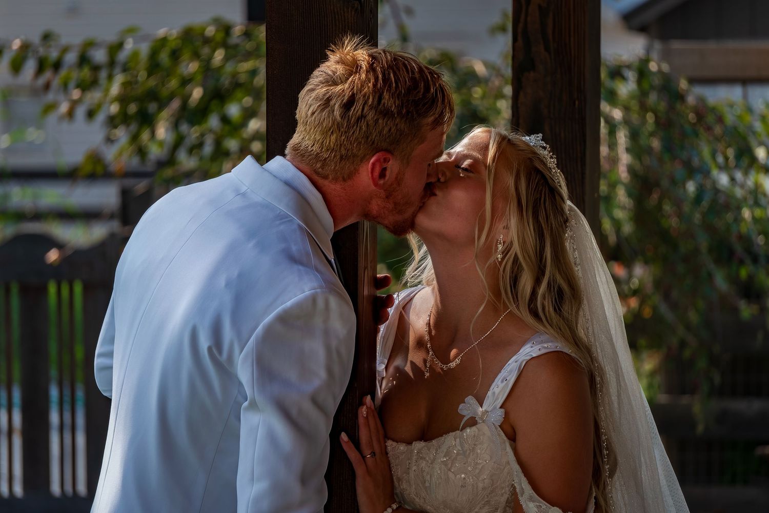 Intimate wedding kiss shared under rustic wooden pergola at sunset.