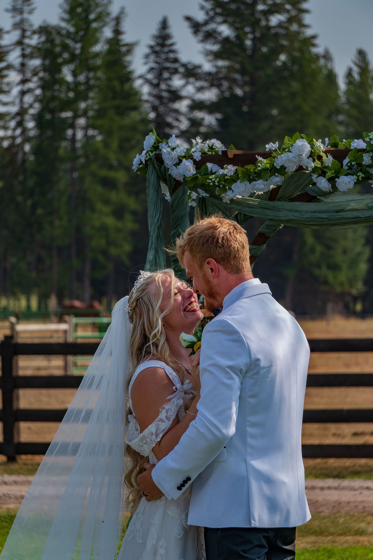 Wedding couple's passionate first kiss with pine forest and wooden fence in background.