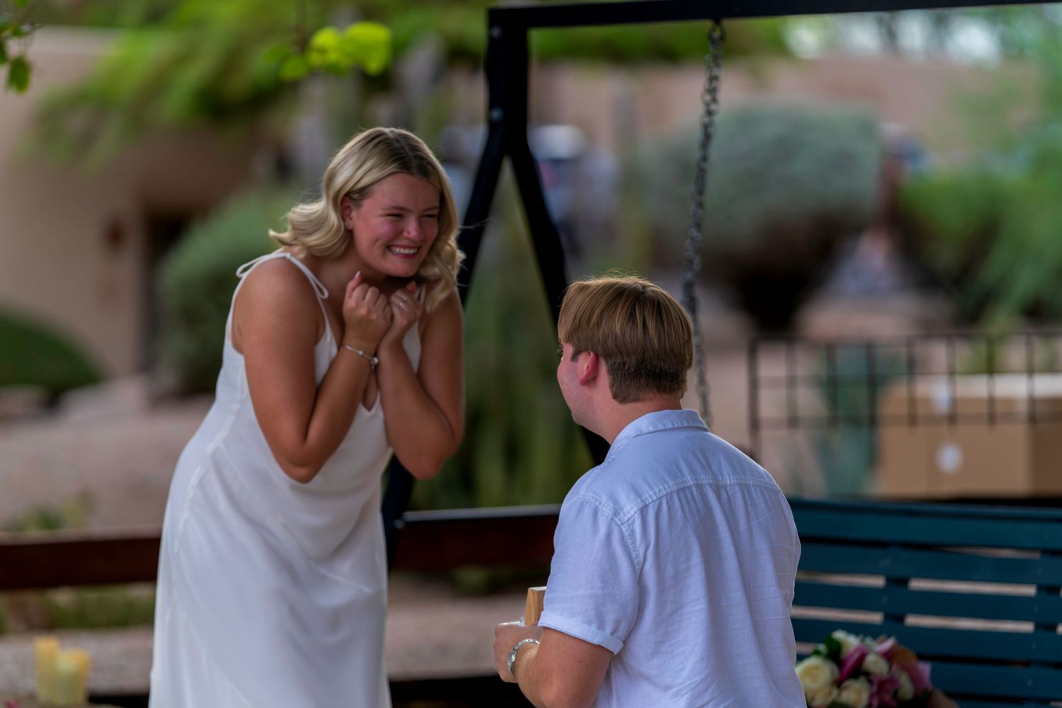 Couple sharing a joyful engagement moment outdoors near a swing bench.