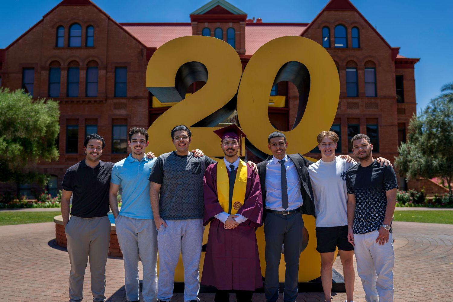 Group of seven people posing in front of large golden 20 numbers at Arizona State University graduation.