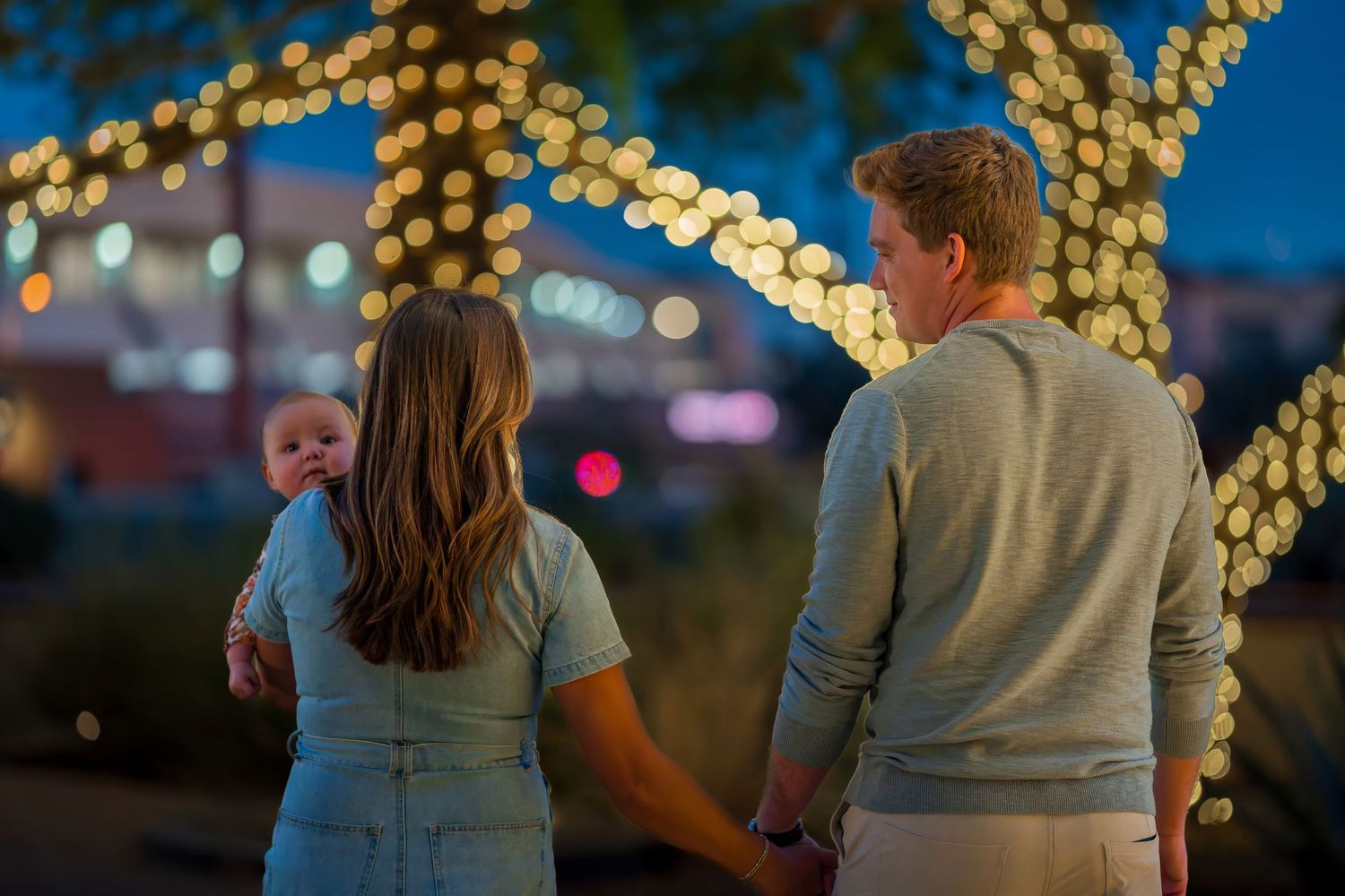Young family with baby enjoying holiday lights display together at night outdoors.