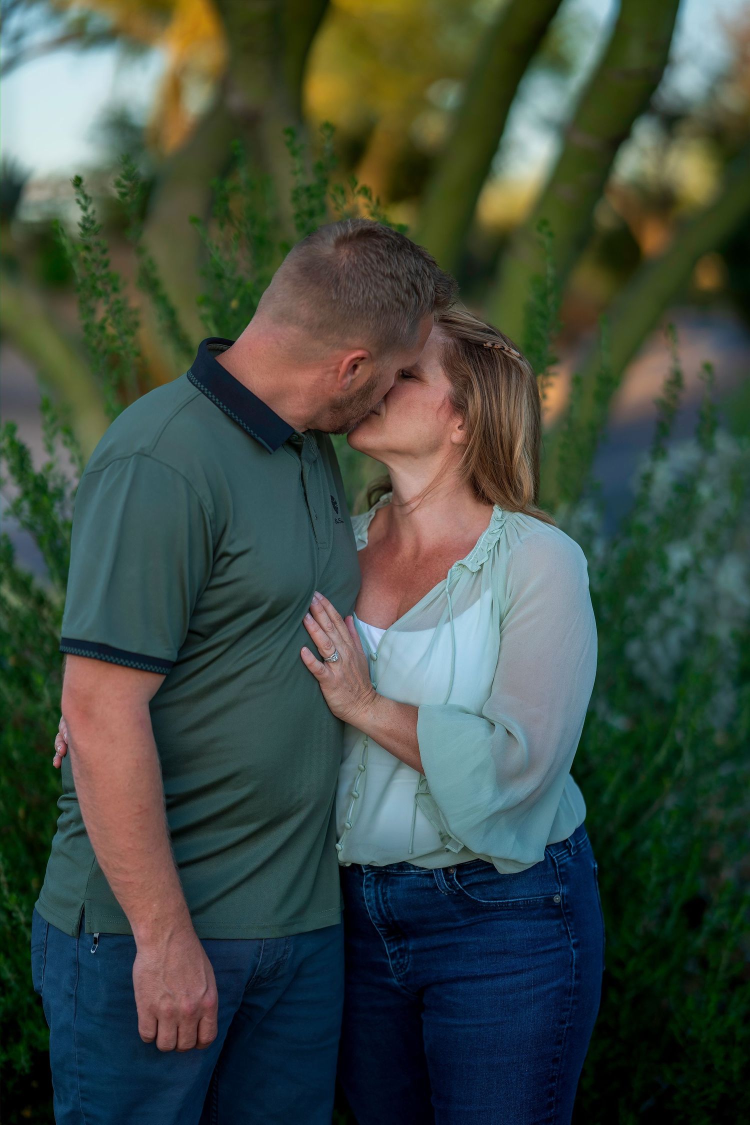 Couple sharing a kiss outdoors surrounded by green plants in warm evening light.