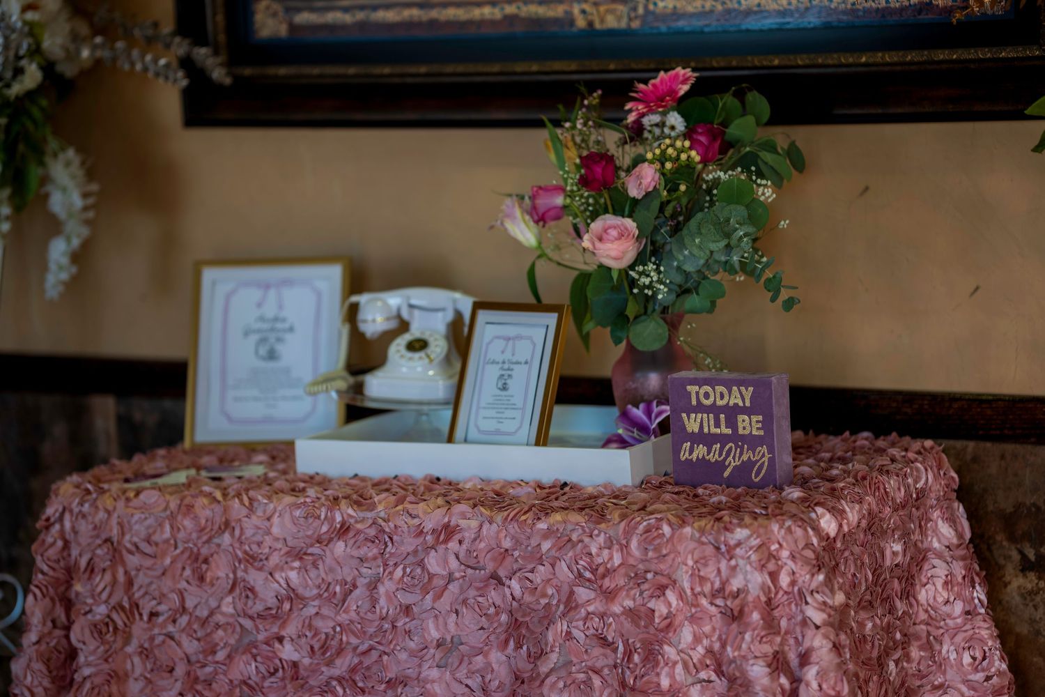 Wedding table with pink floral tablecloth, roses bouquet, framed photos, and inspirational sign reading Today Will Be Amazing.